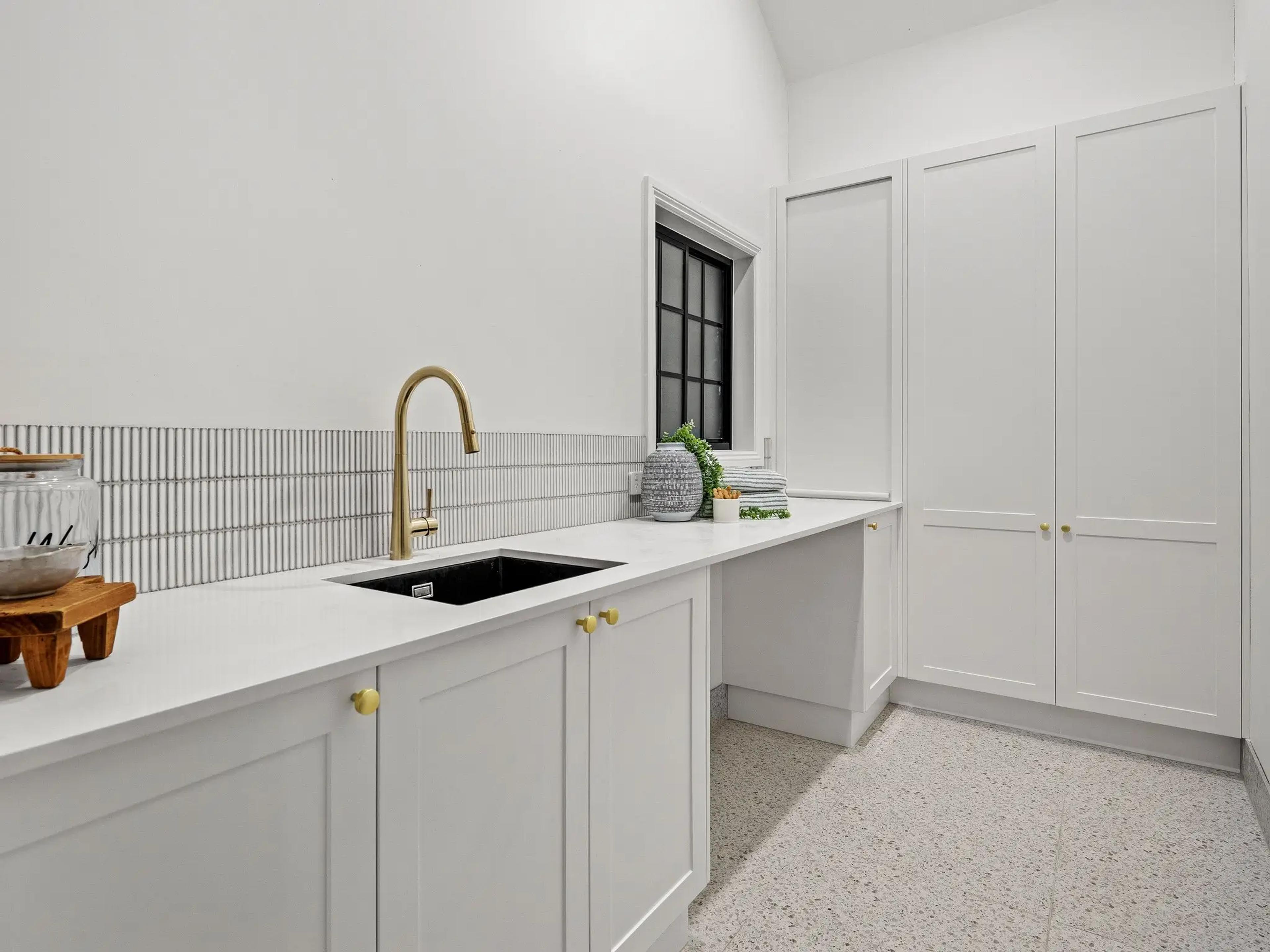 Laundry with brass tapware and white cabinetry