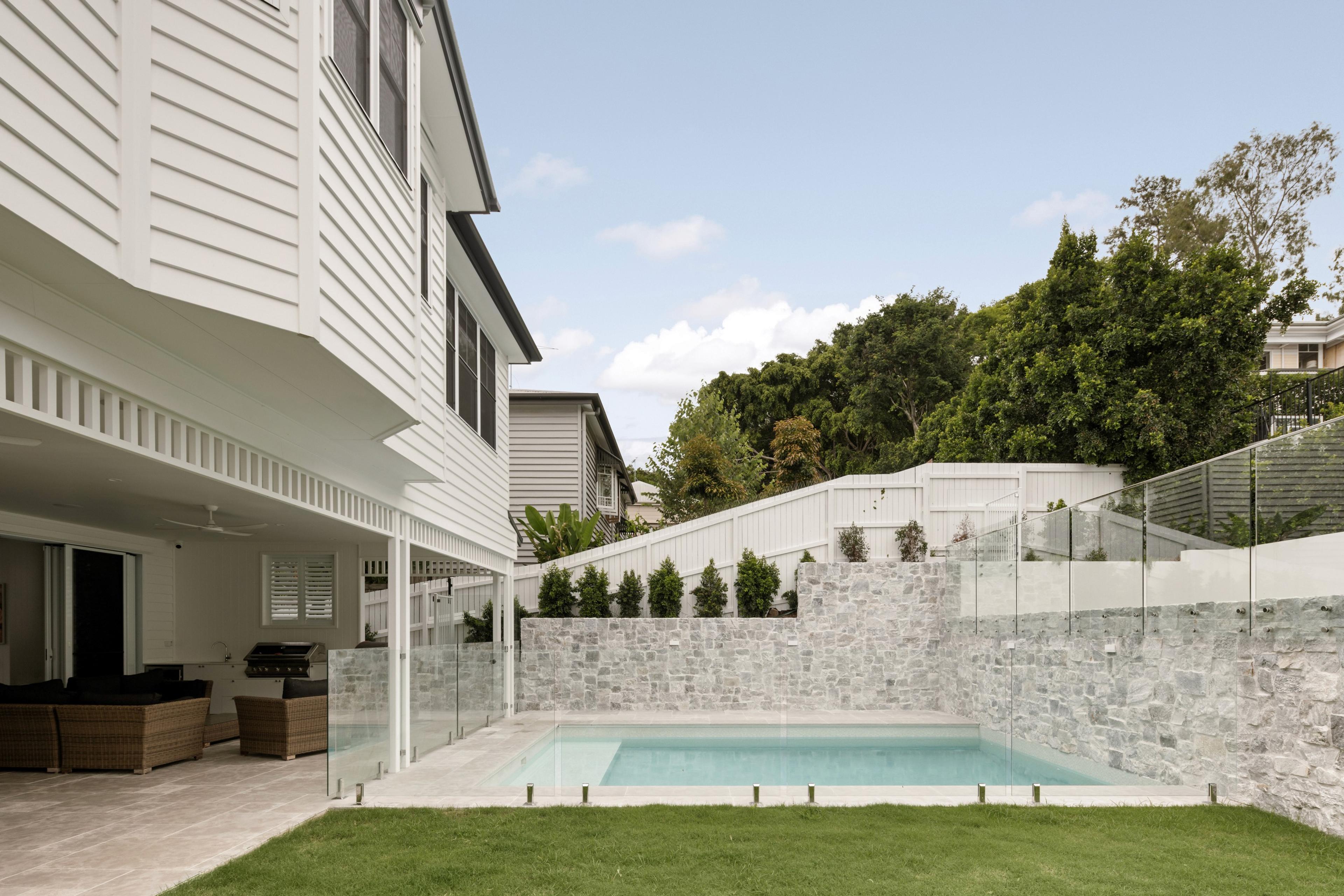 Backyard pool with stone wall and glass fencing