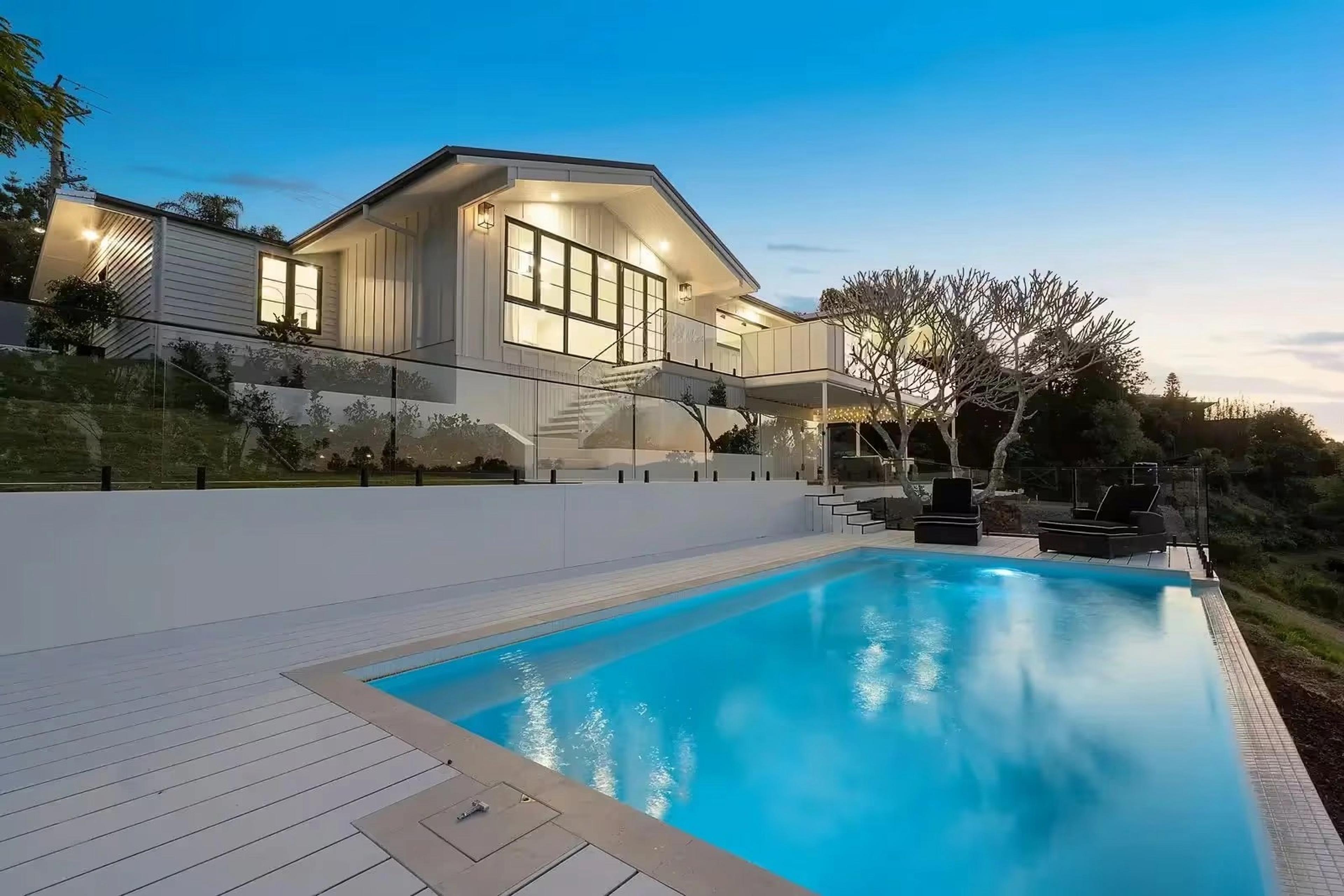 Rear exterior at dusk with illuminated pool and glass fencing.