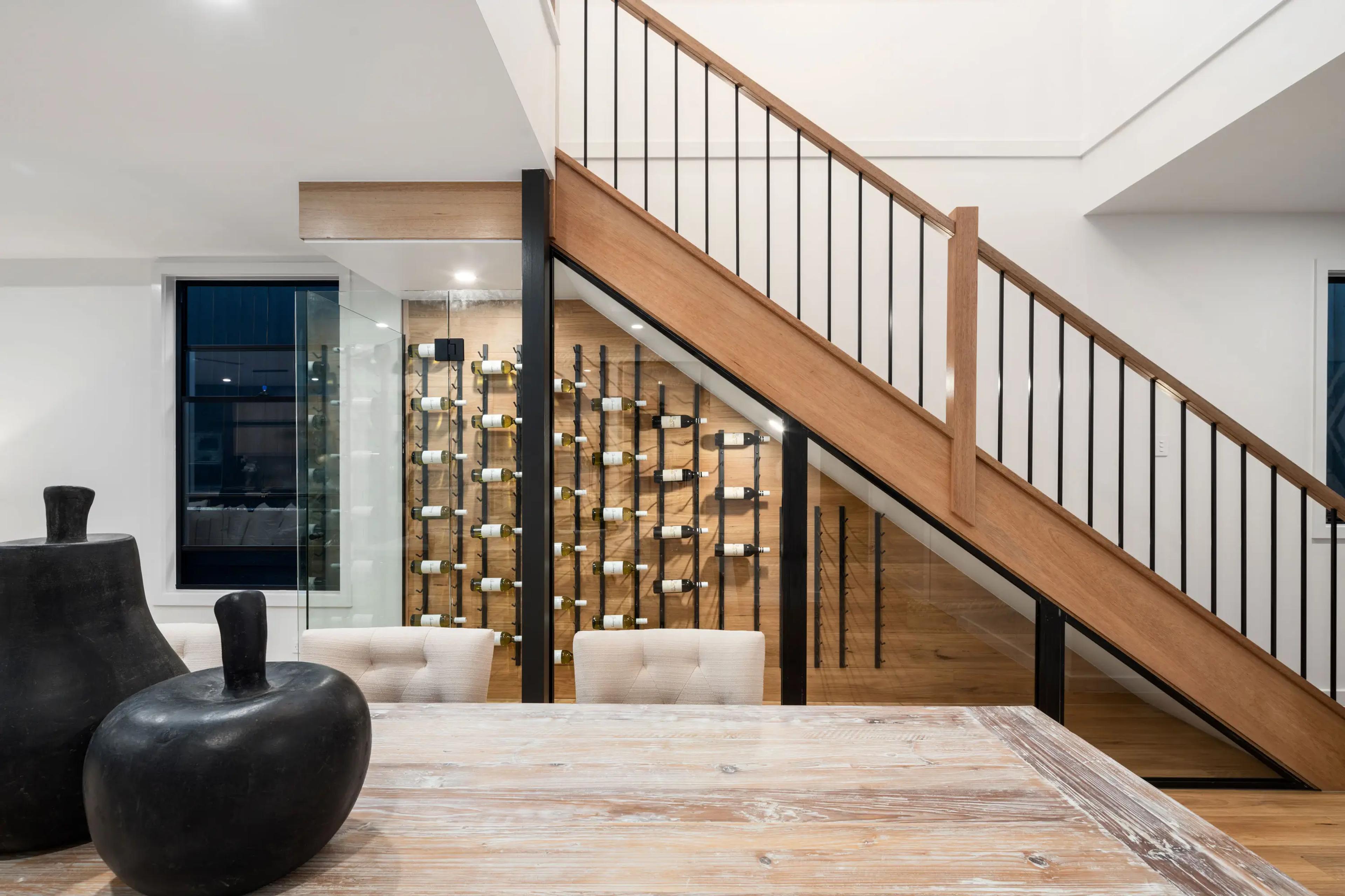 Timber staircase beside glass wine cellar with feature lighting