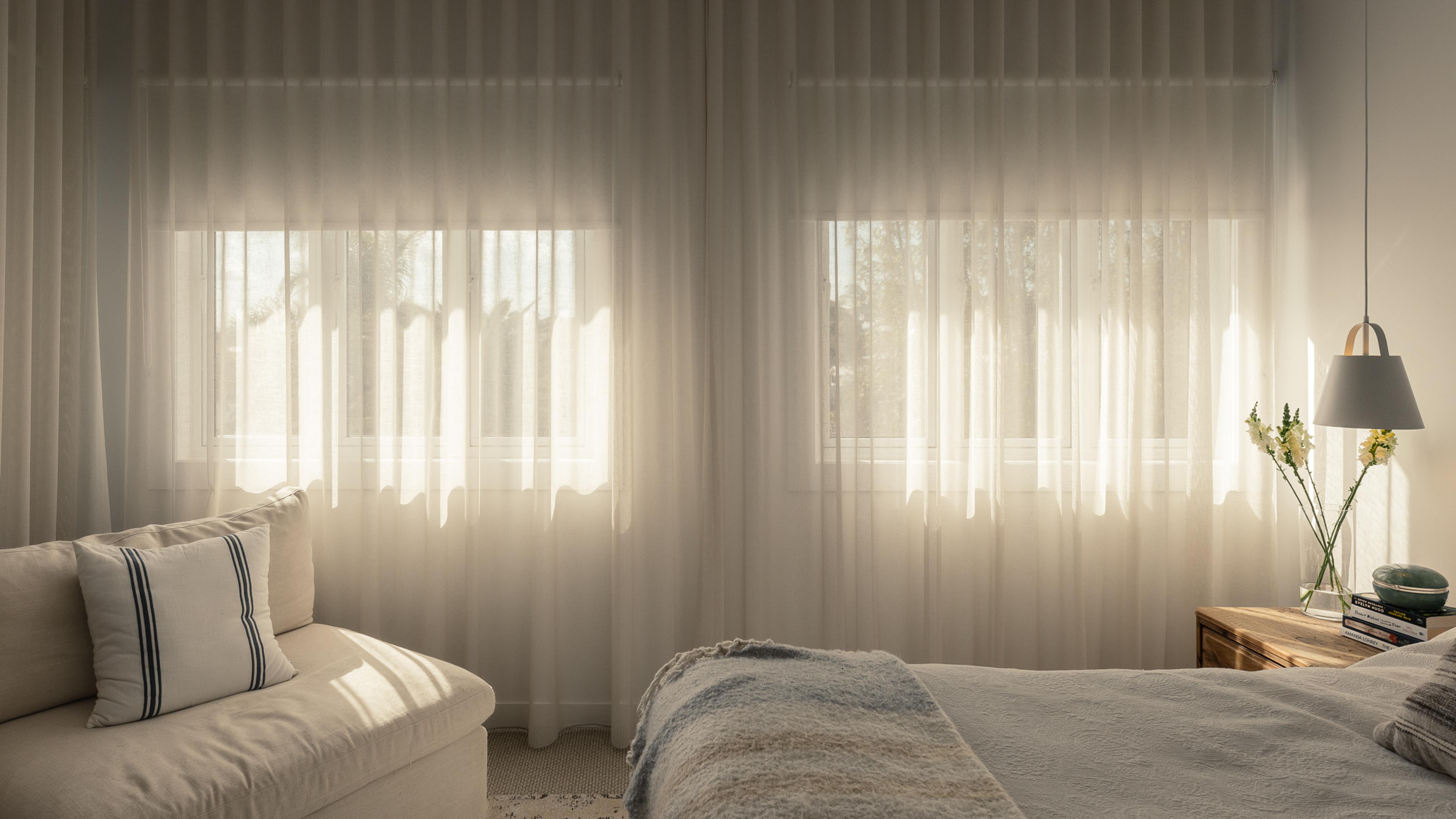 Bedroom with ceiling-height sheer curtains over twin windows and a pendant beside the bed