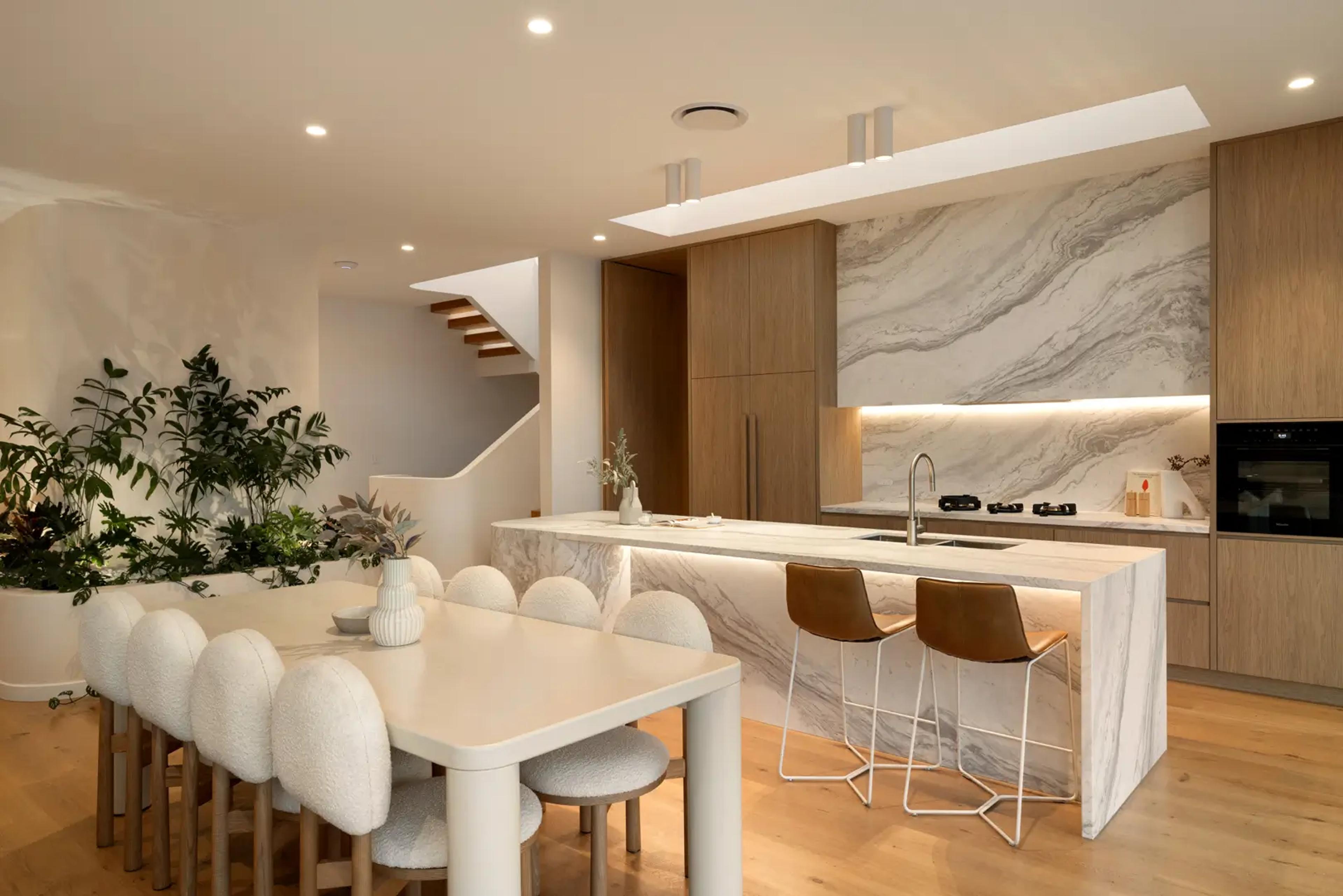 Dining table beside marble kitchen and timber staircase