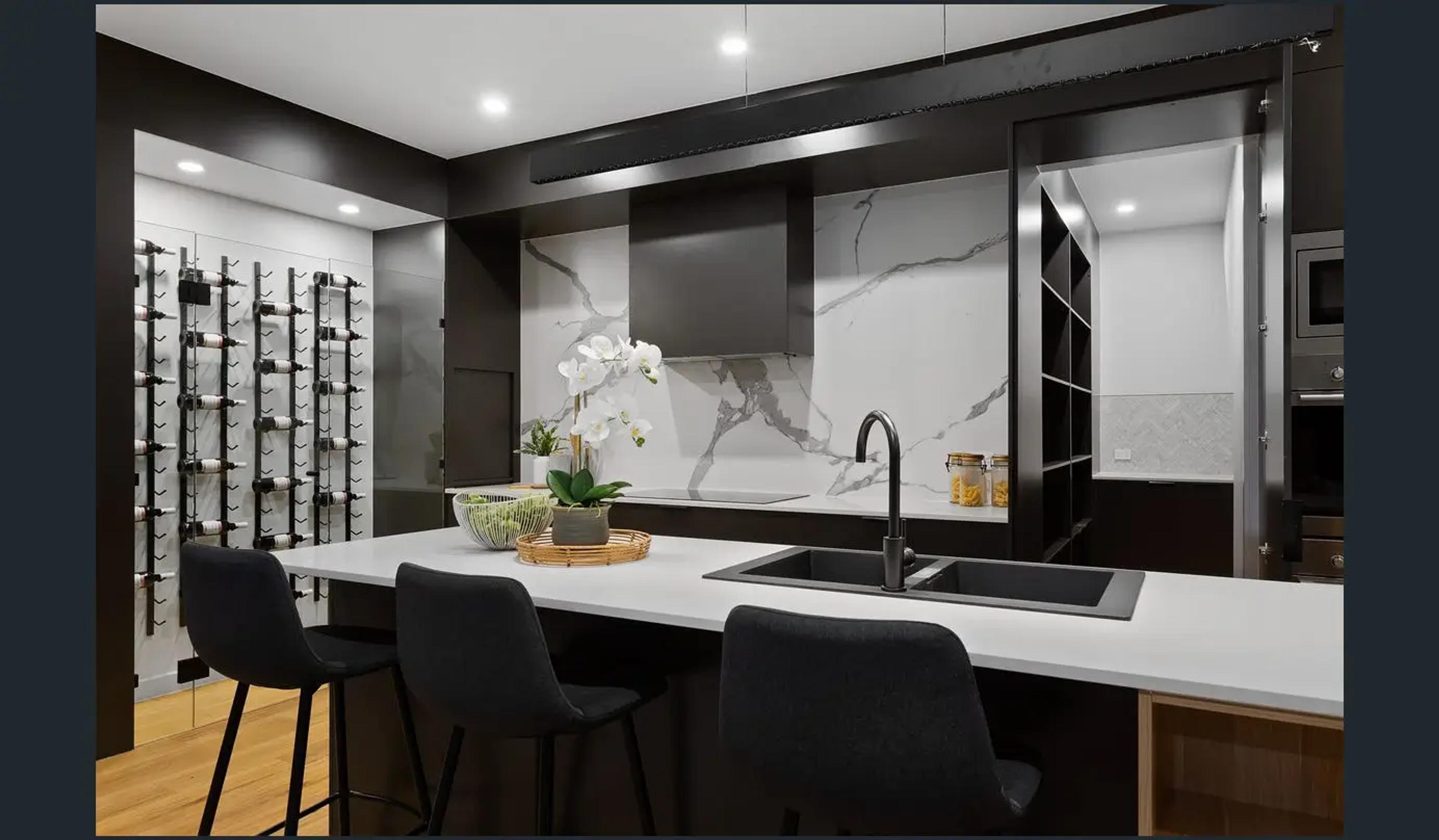 Dark kitchen with marble splashback, island bench and wine wall
