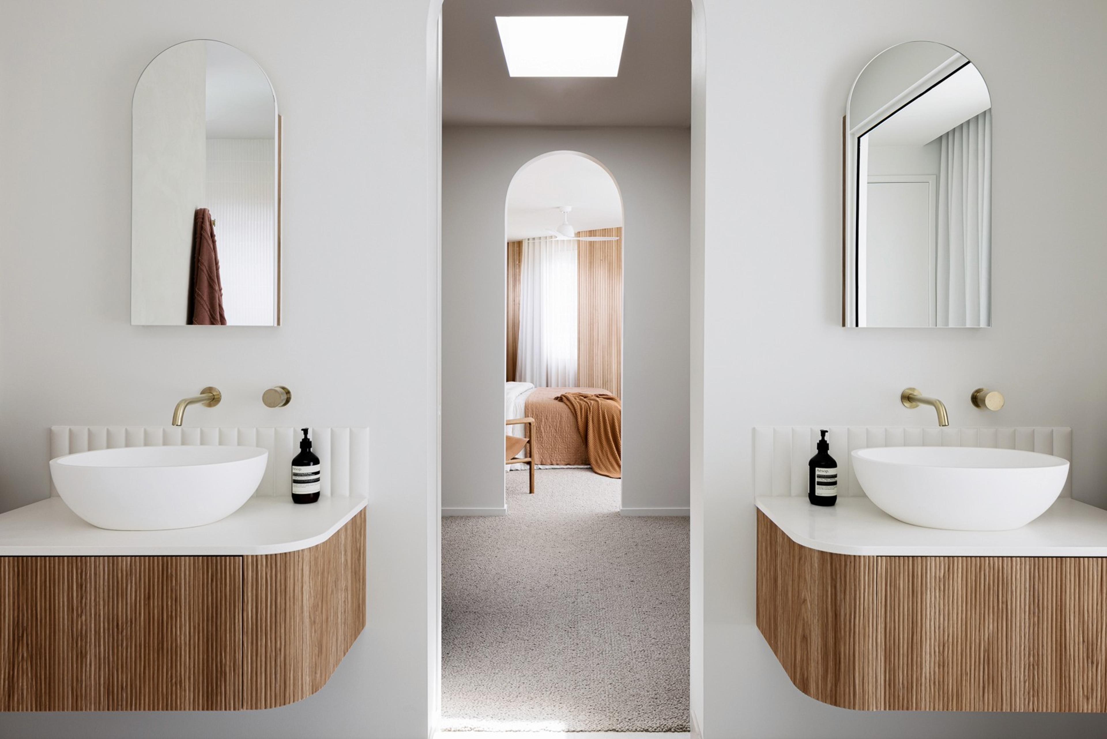 Twin timber vanities with arched mirrors and brass tapware