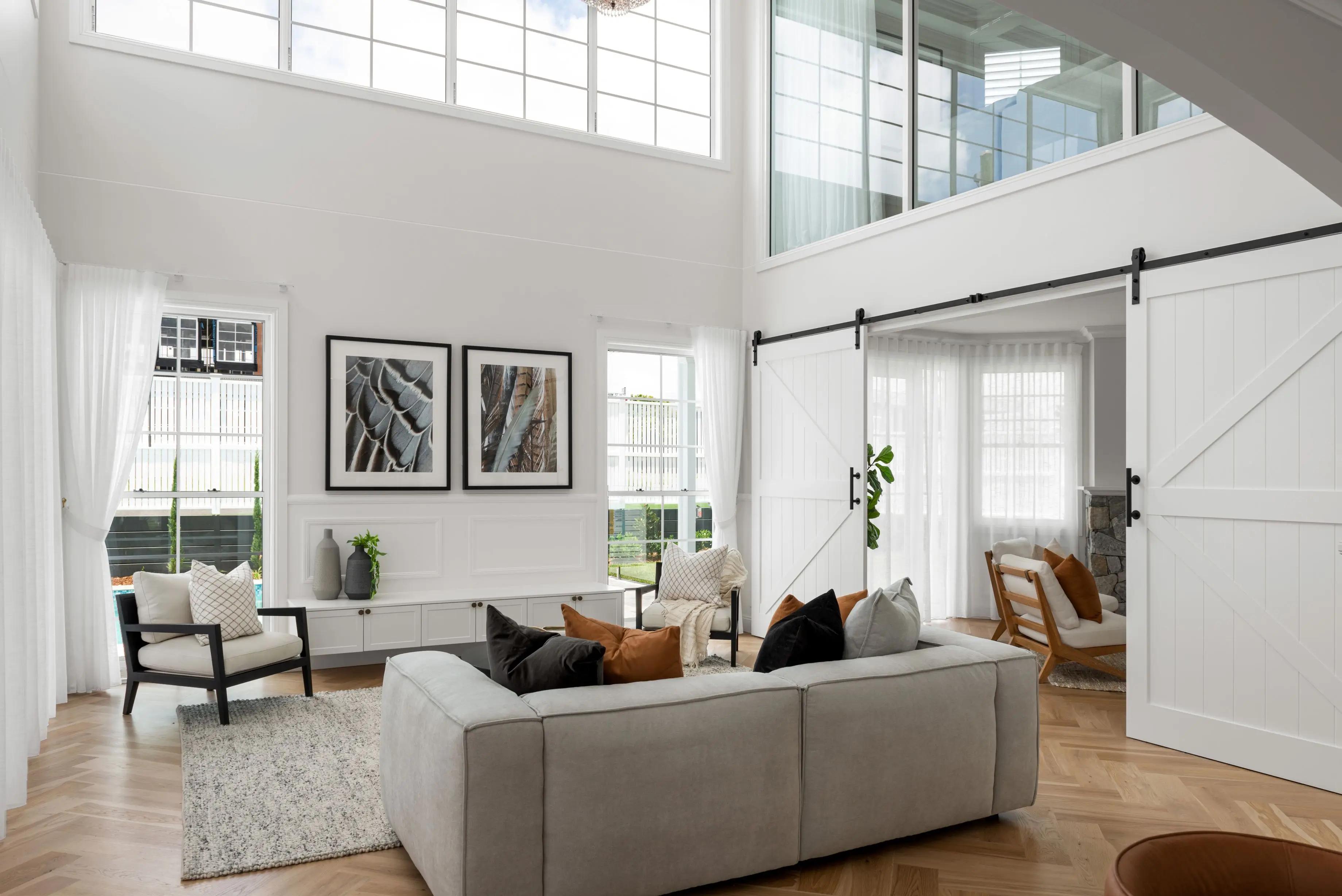 Modern architectural living space demonstrating the principles of light-reflective design with white walls, polished herringbone wood flooring, and sheer curtains to amplify natural light penetration.