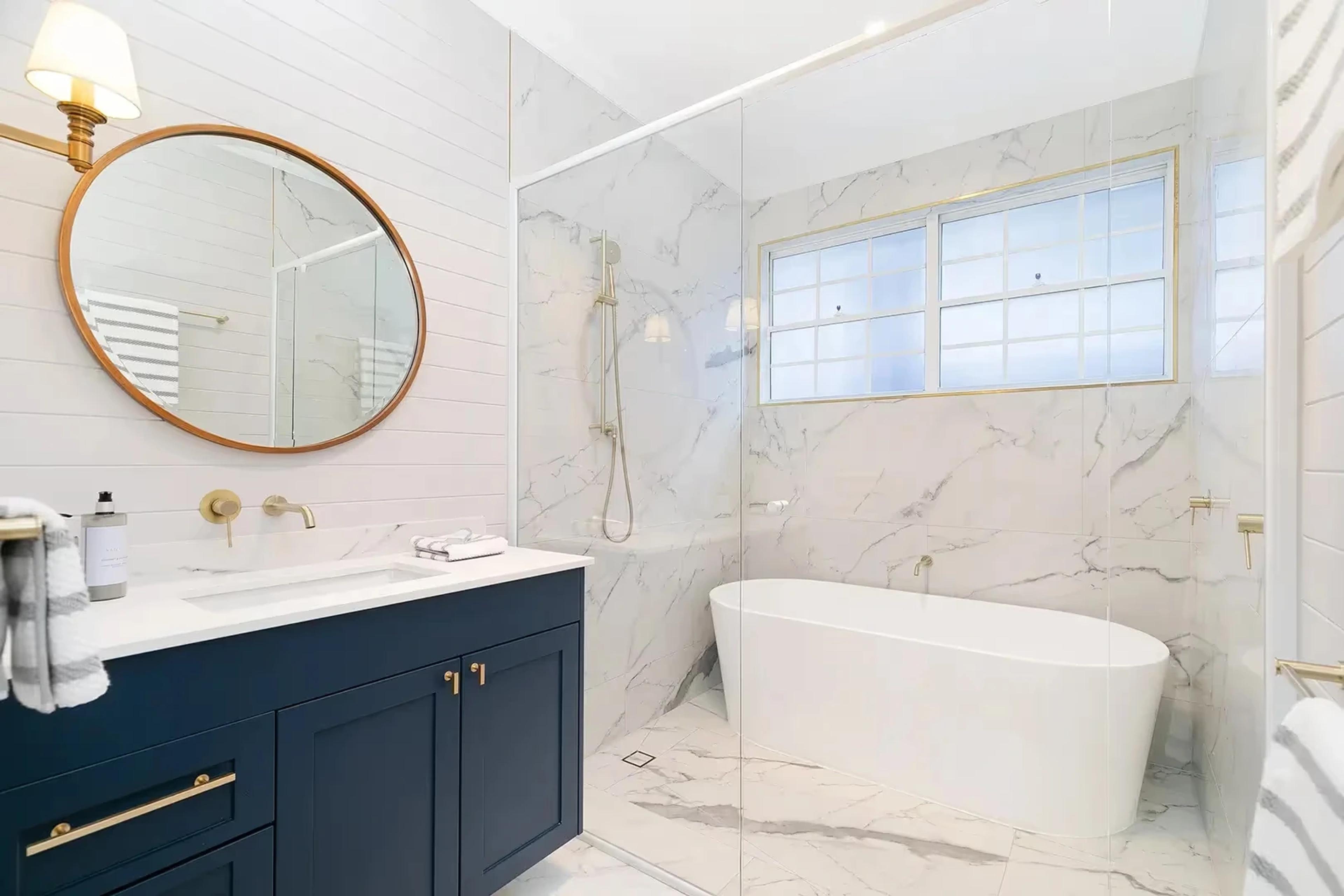 Bathroom with round mirror, navy vanity and freestanding bath