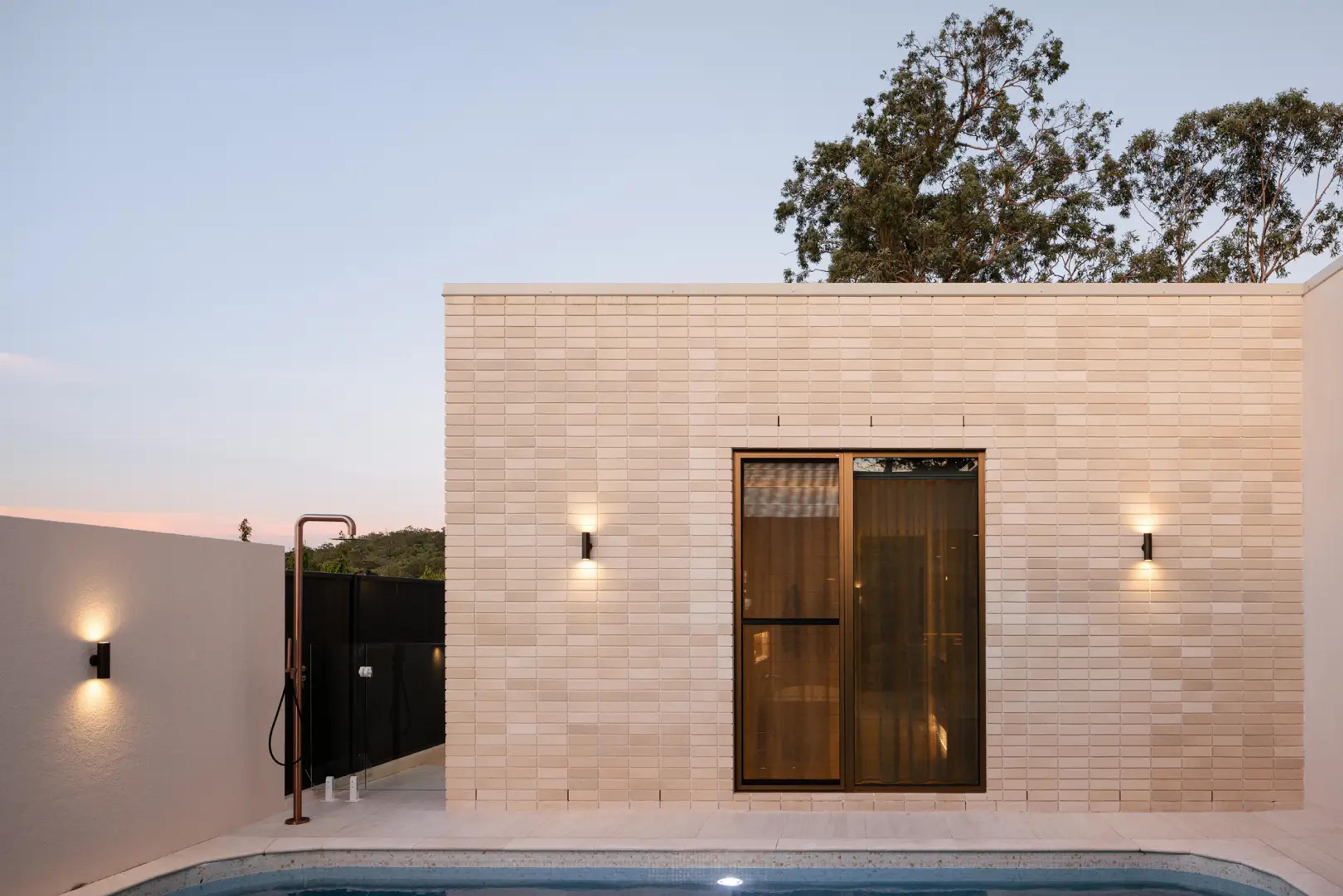 Poolside brick pavilion with wall lights and outdoor shower