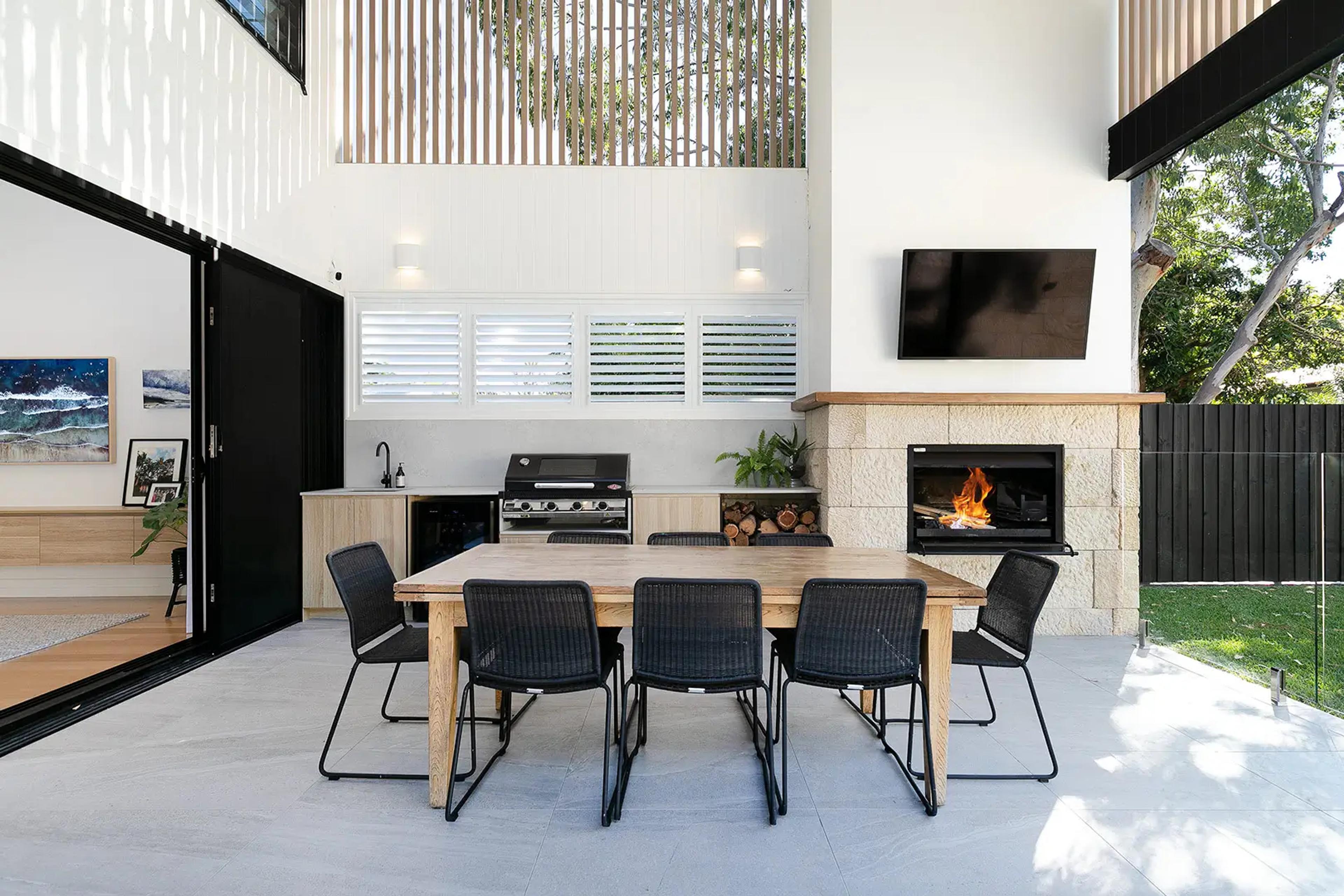 Covered alfresco kitchen with barbecue, dining table and stone fireplace