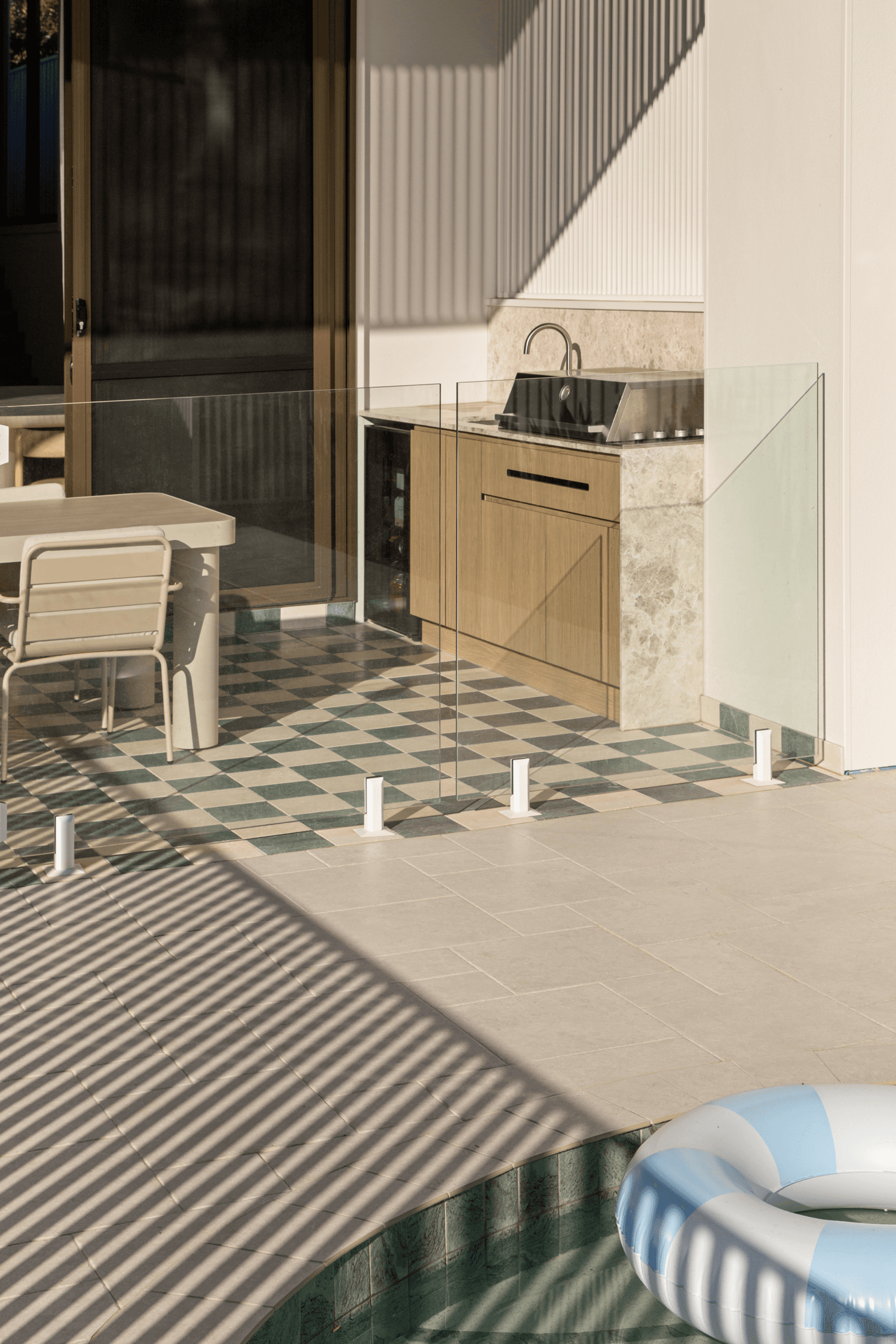 Outdoor kitchen and dining beside pool on chequered tiles