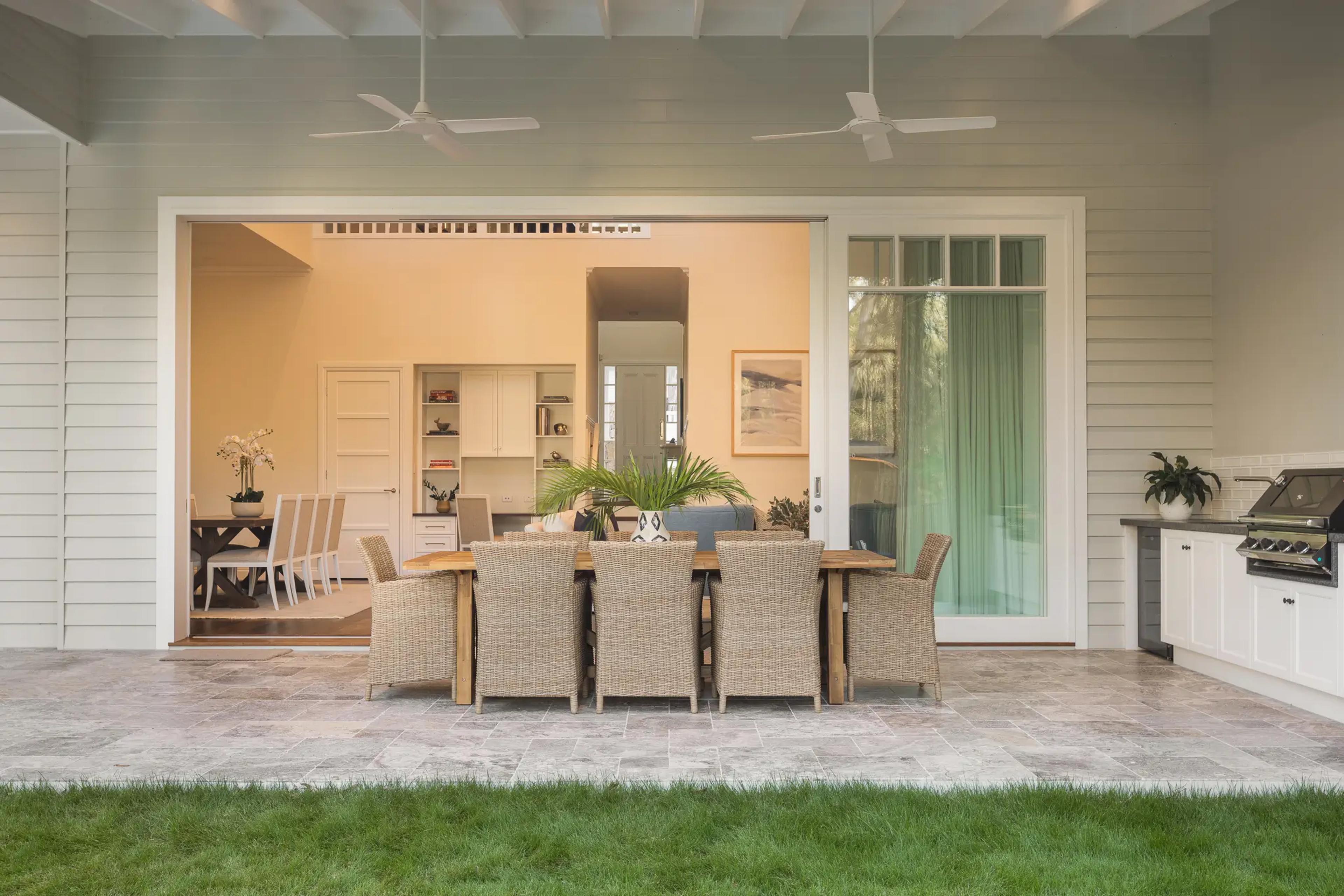 Covered alfresco patio with dining table opening onto lawn and living room