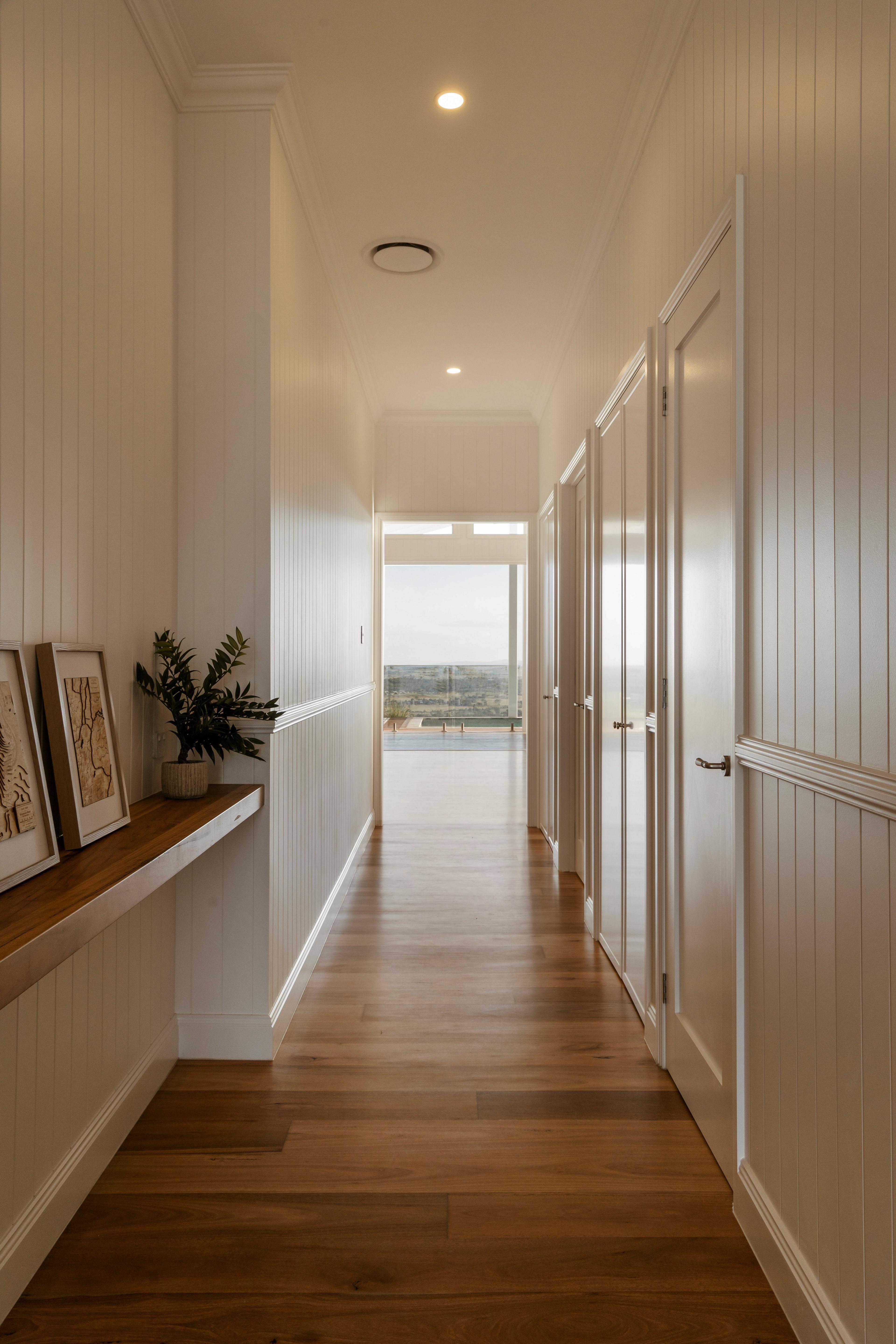 Long hallway with timber floor and framed artwork leading to view