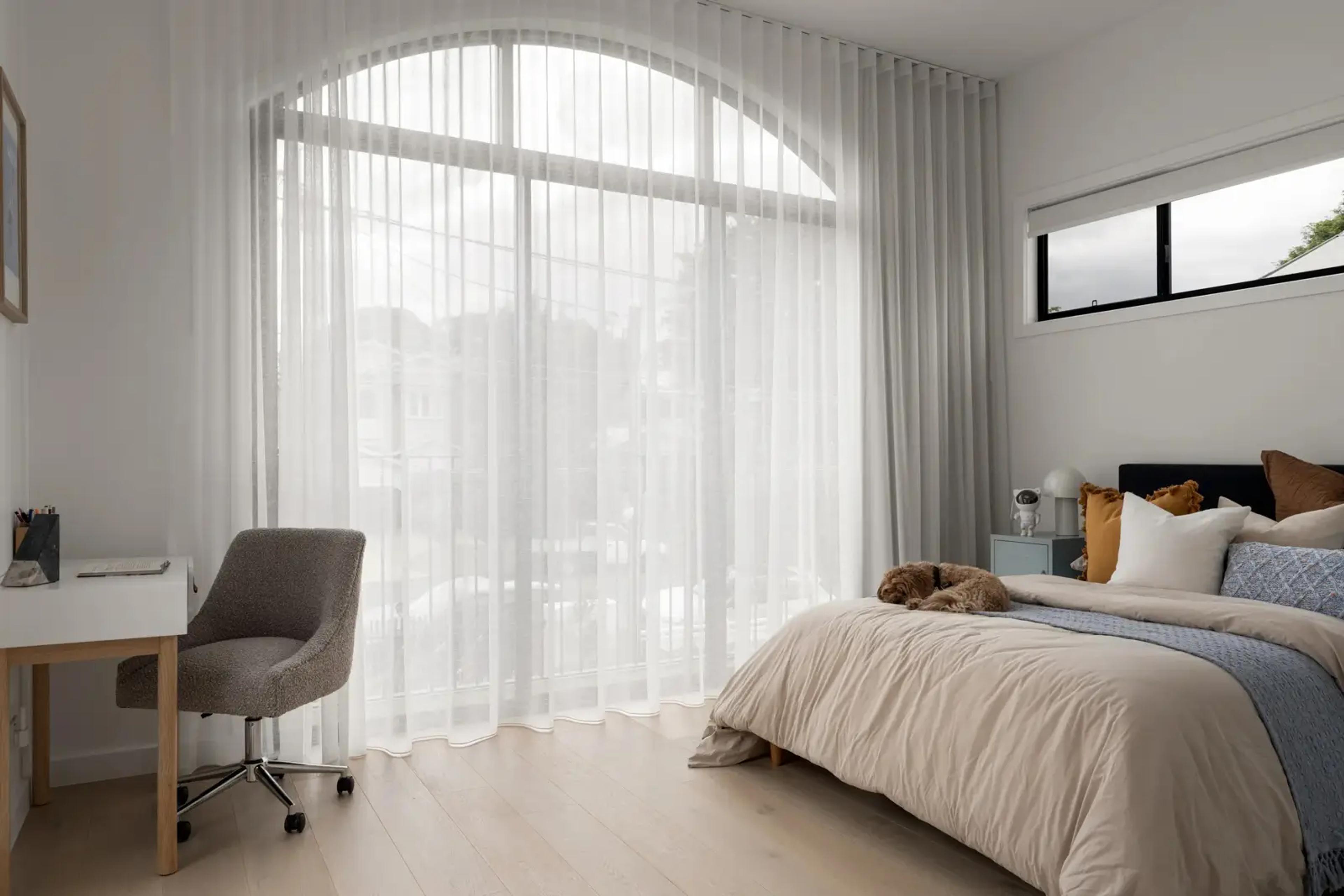 Bedroom with arched sheer curtains, desk and upholstered bedhead