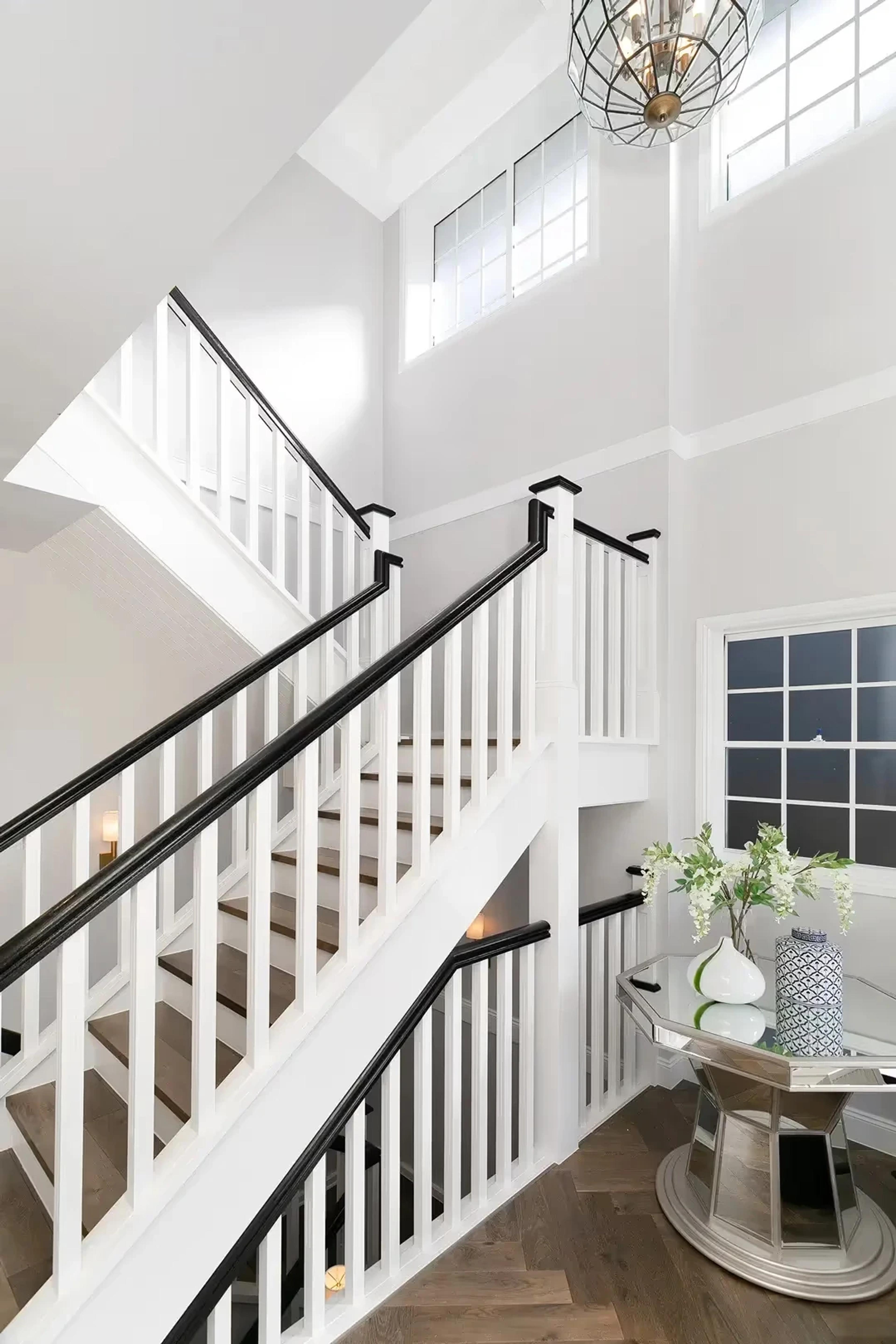 White timber staircase with dark handrails and high windows