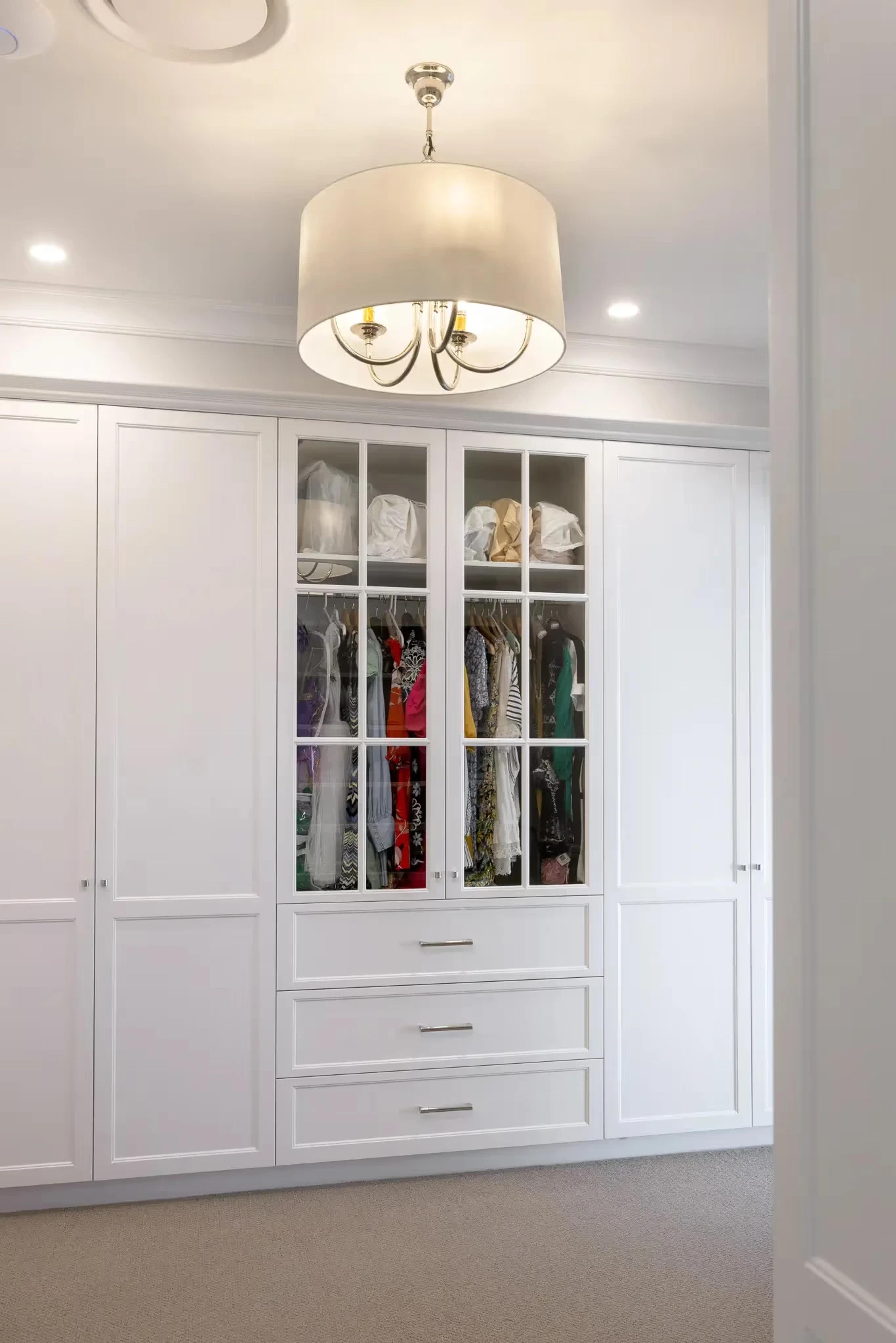 Walk in wardrobe with glass fronted cabinetry and pendant light