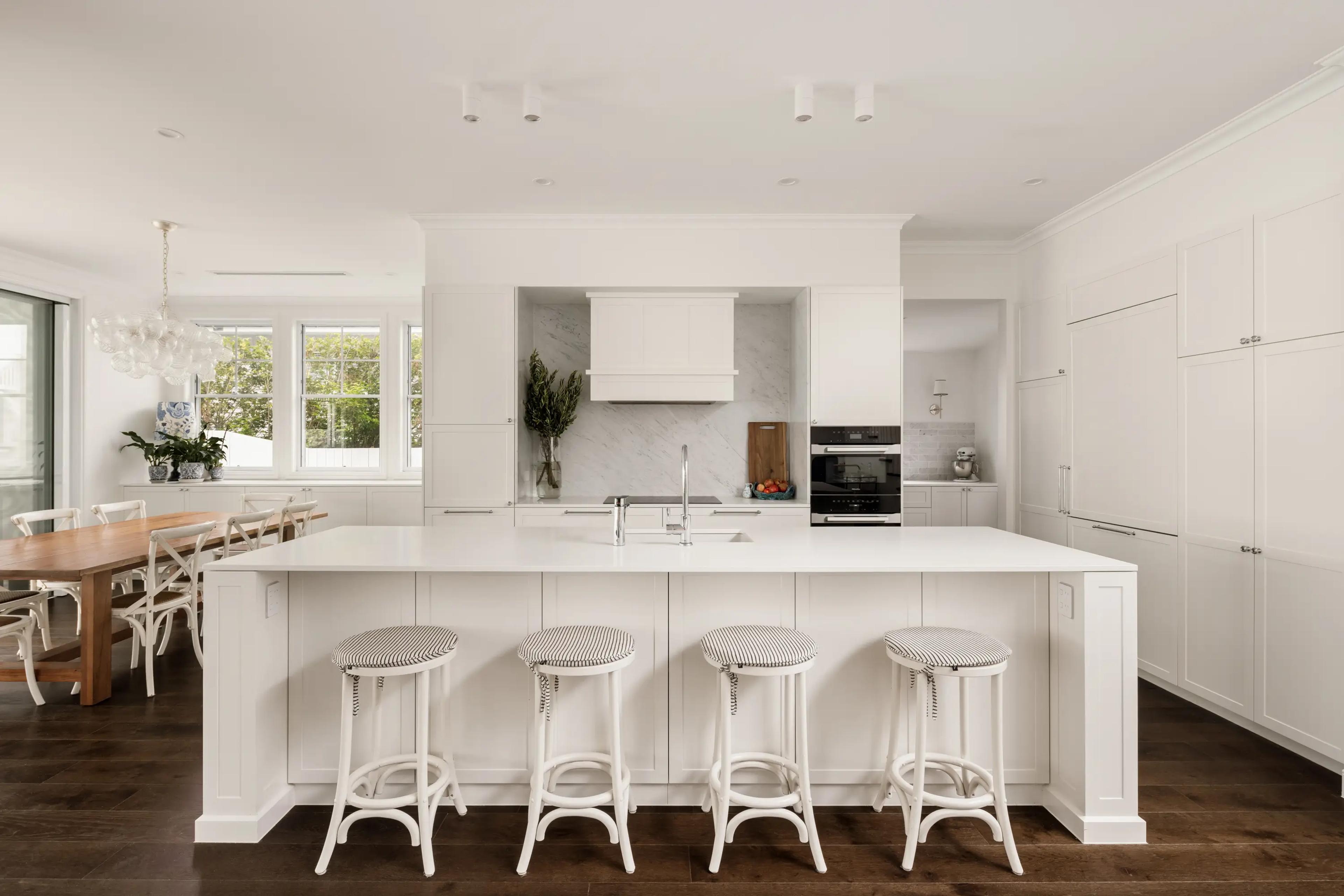 White kitchen with island bench, stools and dining table