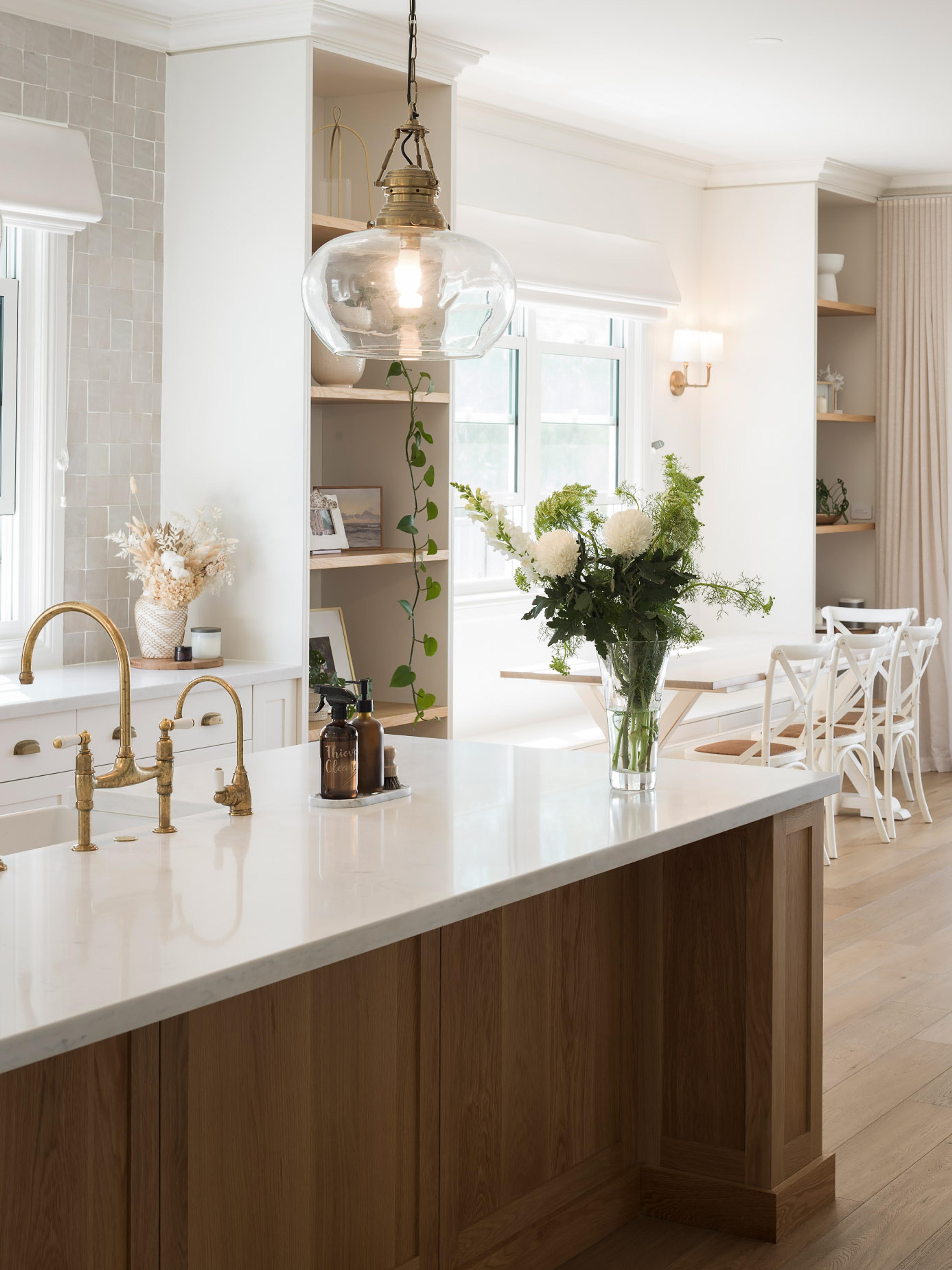 Kitchen island with brass tapware, flowers and dining area beyond