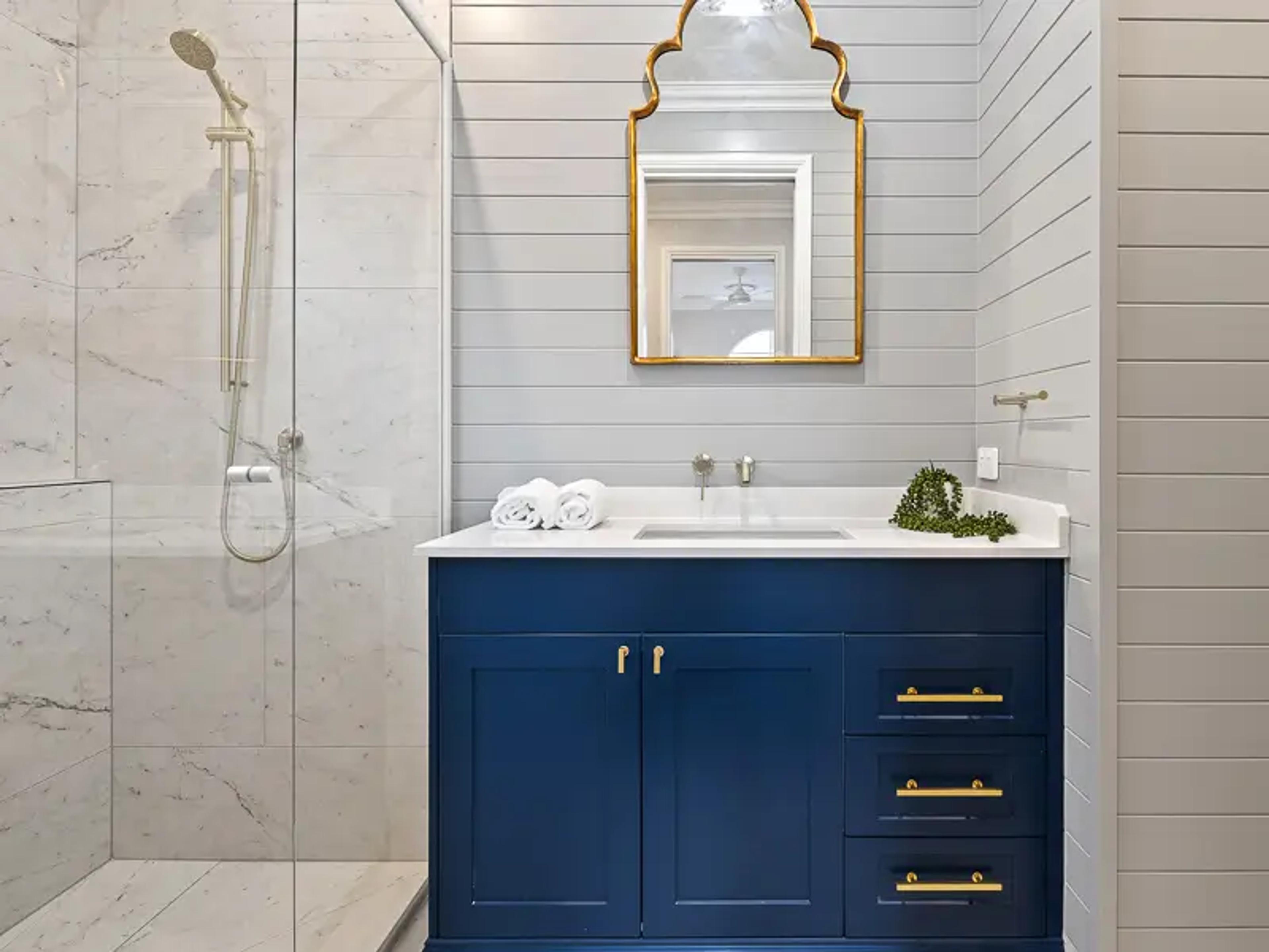Bathroom with navy vanity, gold framed mirror and shower
