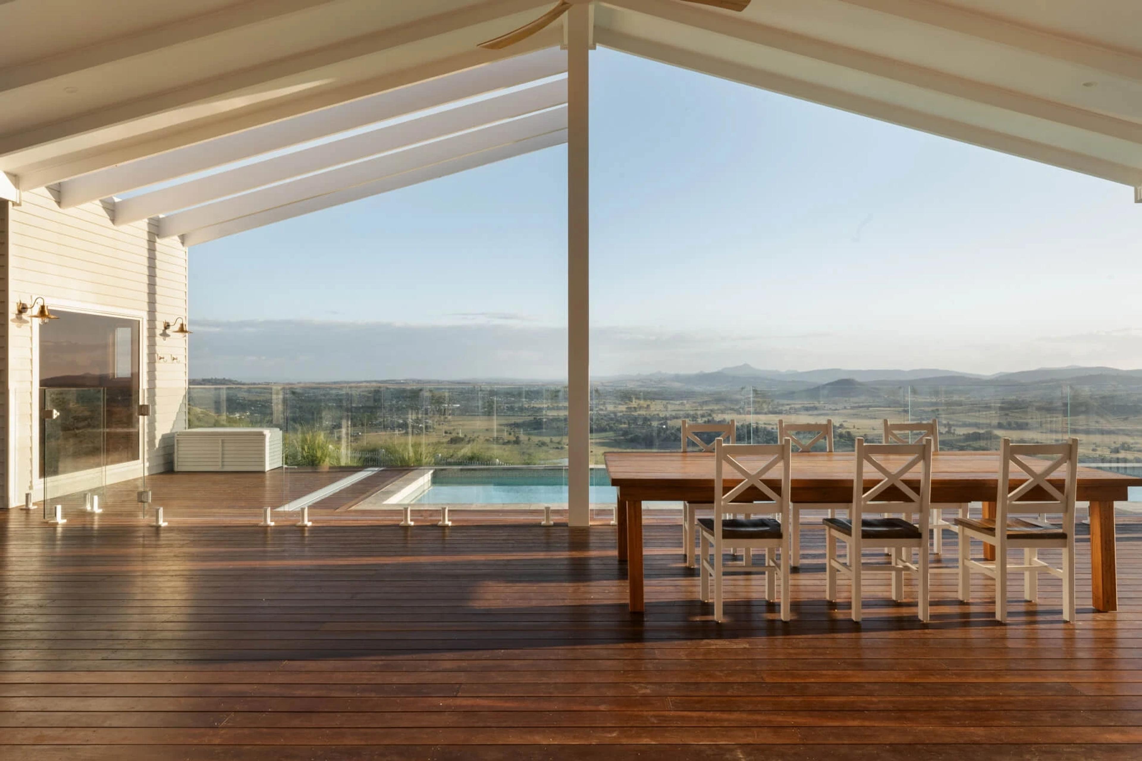 Covered deck with dining table overlooking pool and rural valley