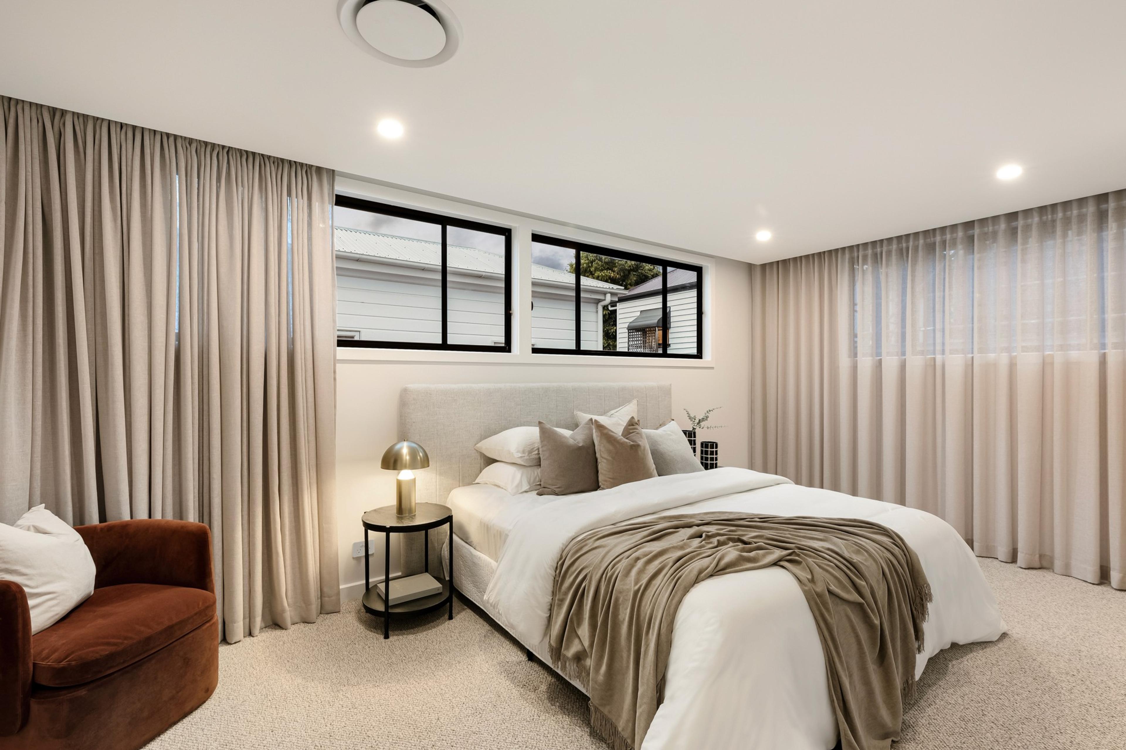 Bedroom with upholstered bed, neutral curtains and clerestory windows