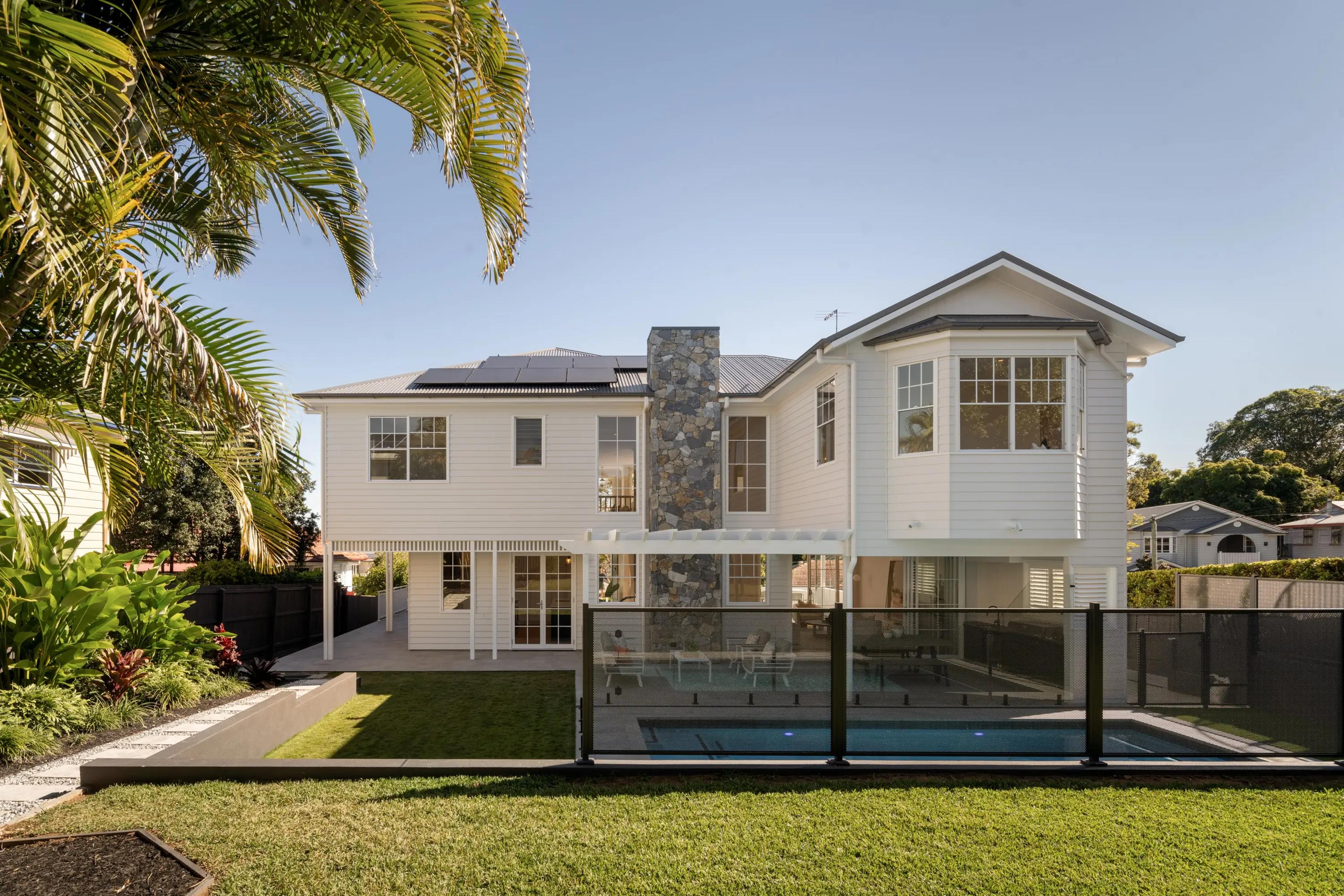 Rear exterior of white home with stone chimney and pool