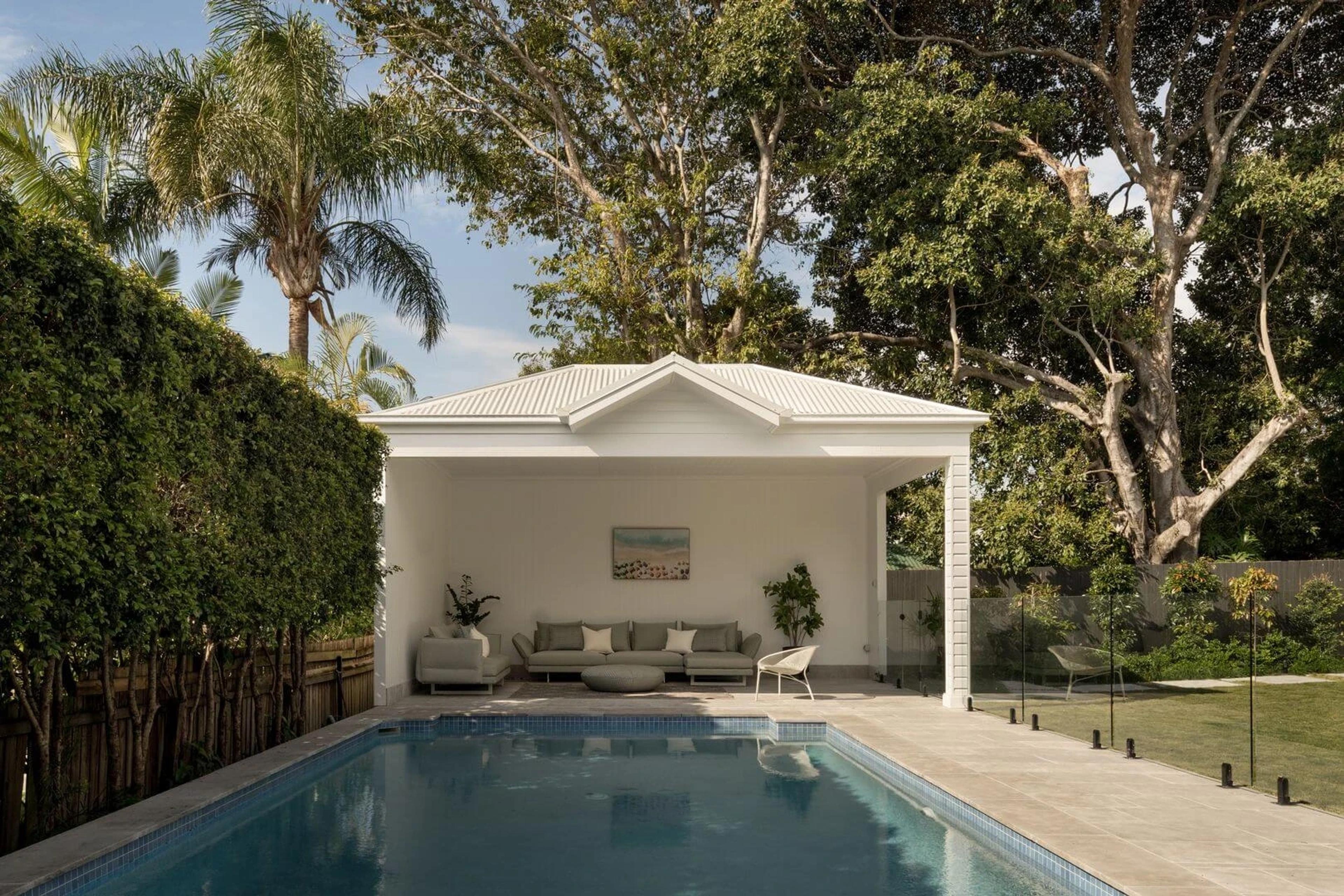 Swimming pool beside white poolside pavilion with lounge seating