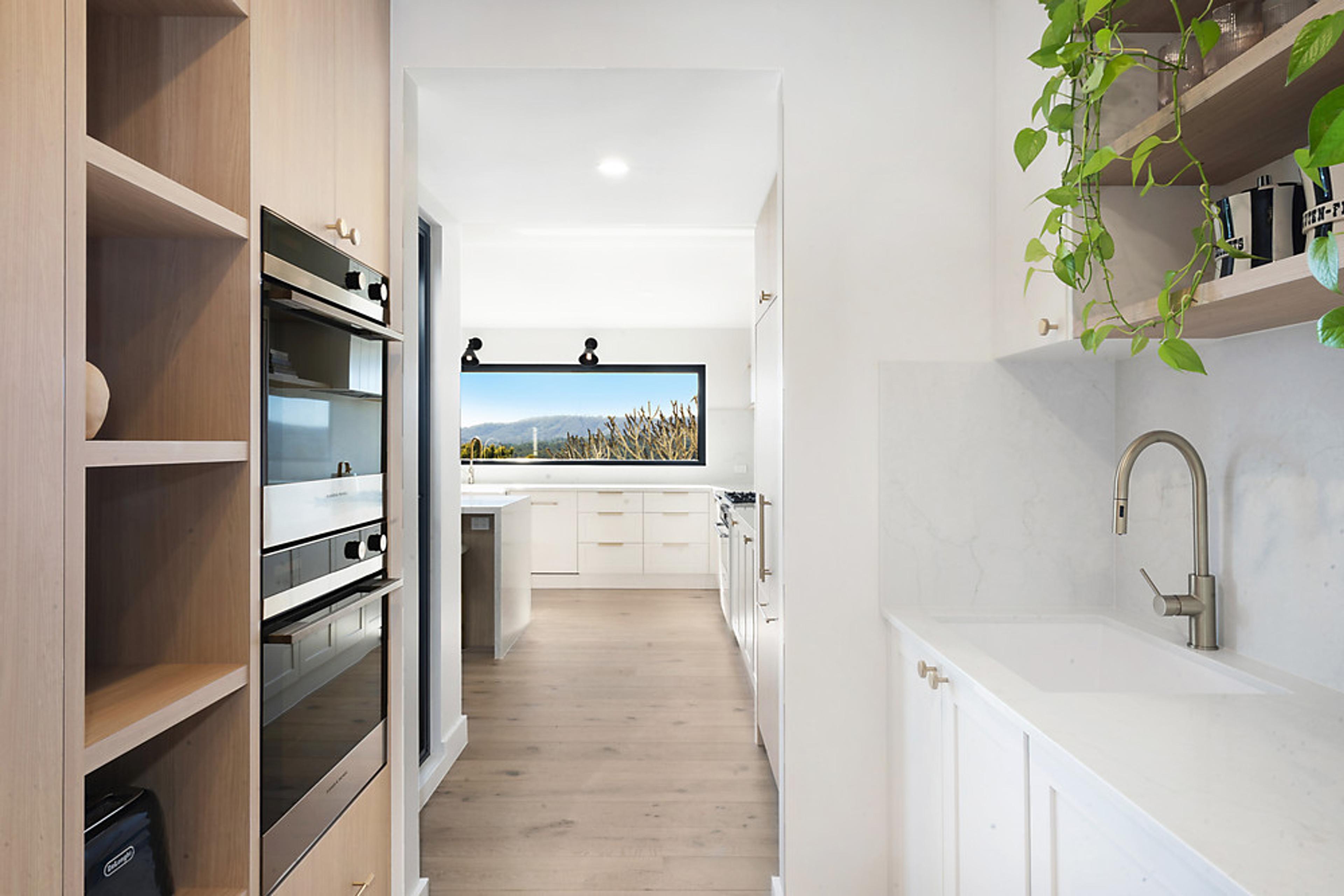 Butler’s pantry with timber joinery and double ovens, looking through to the kitchen
