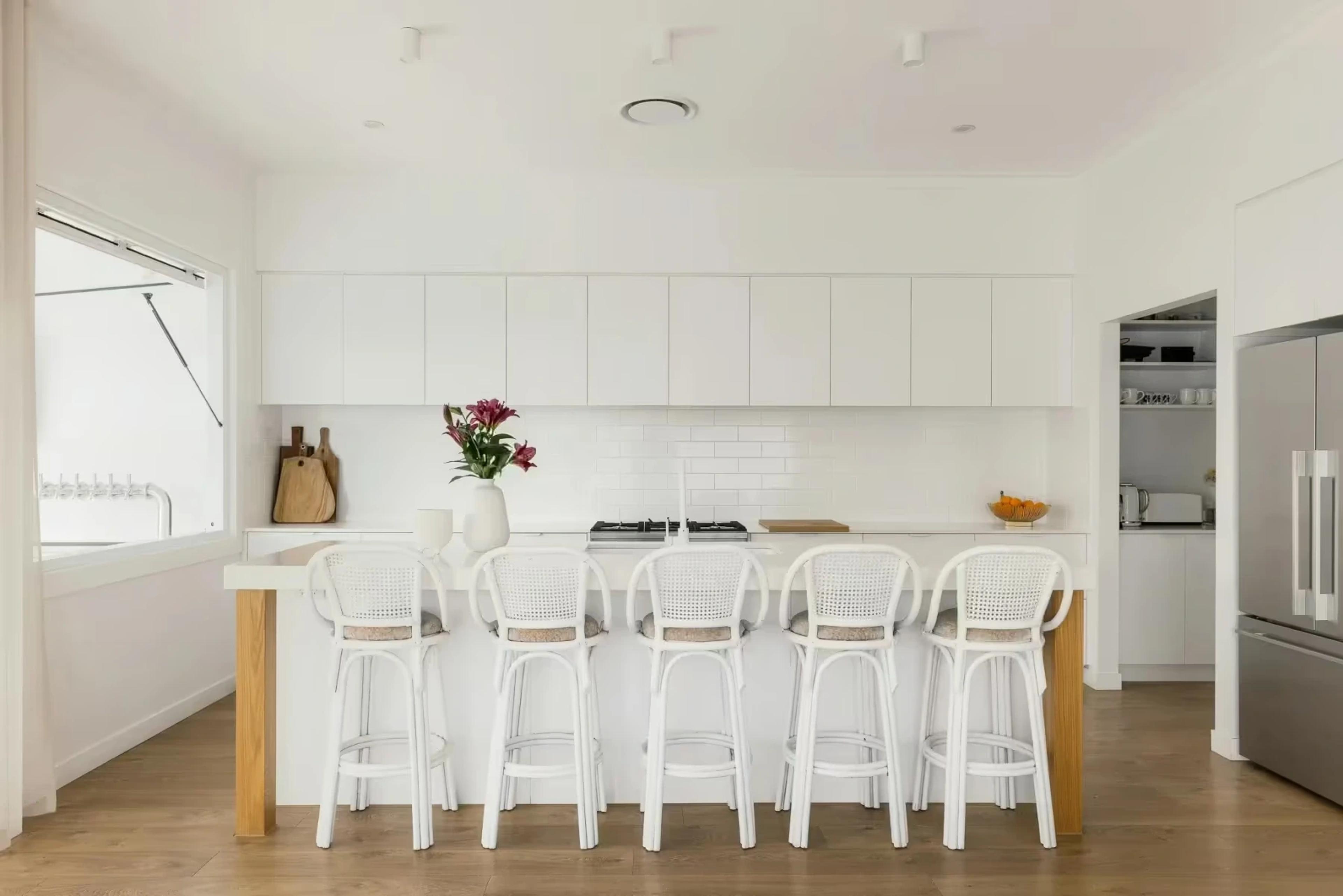 White kitchen with island bench and rattan bar stools