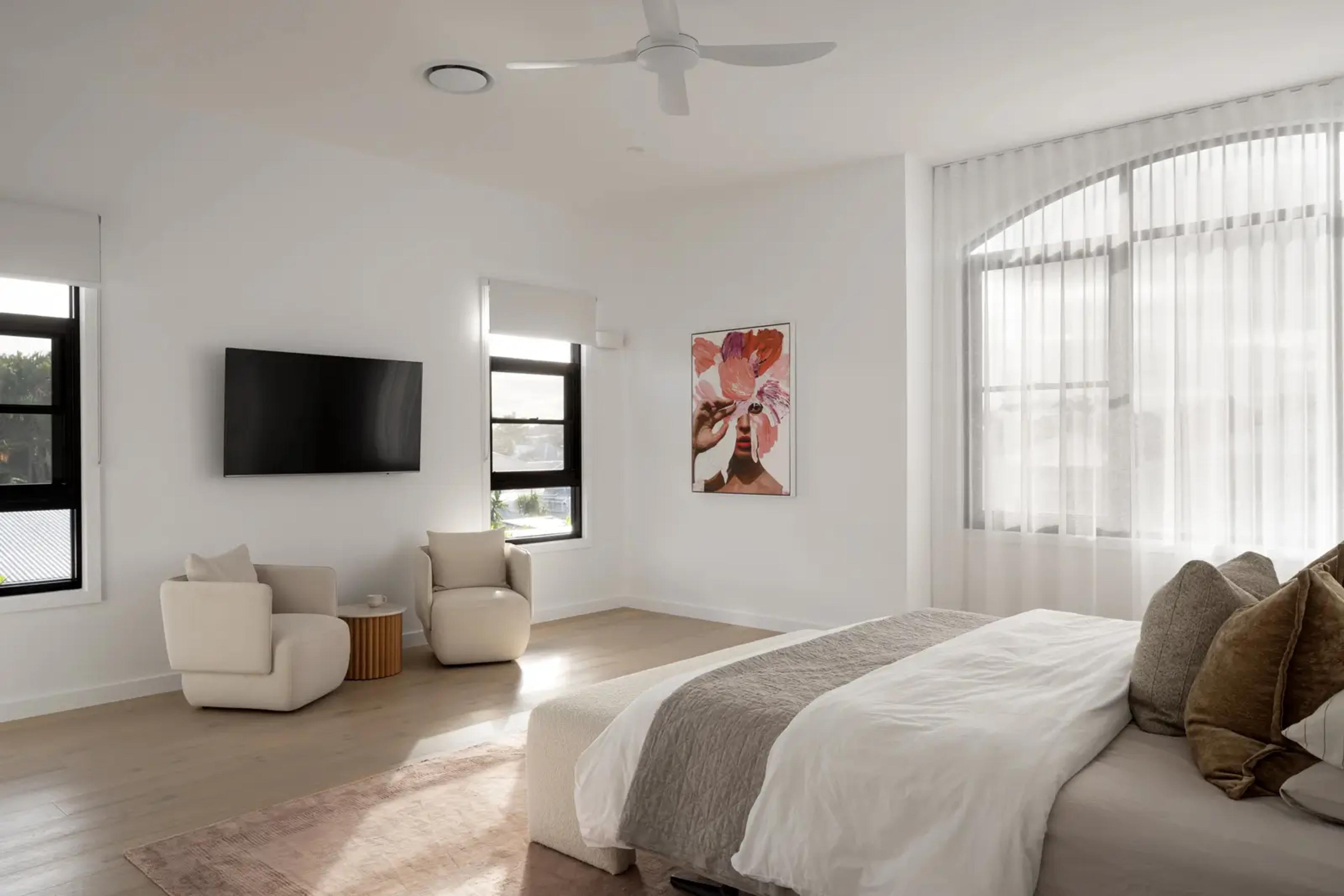 Main bedroom with arched sheer curtained window and wall mounted television