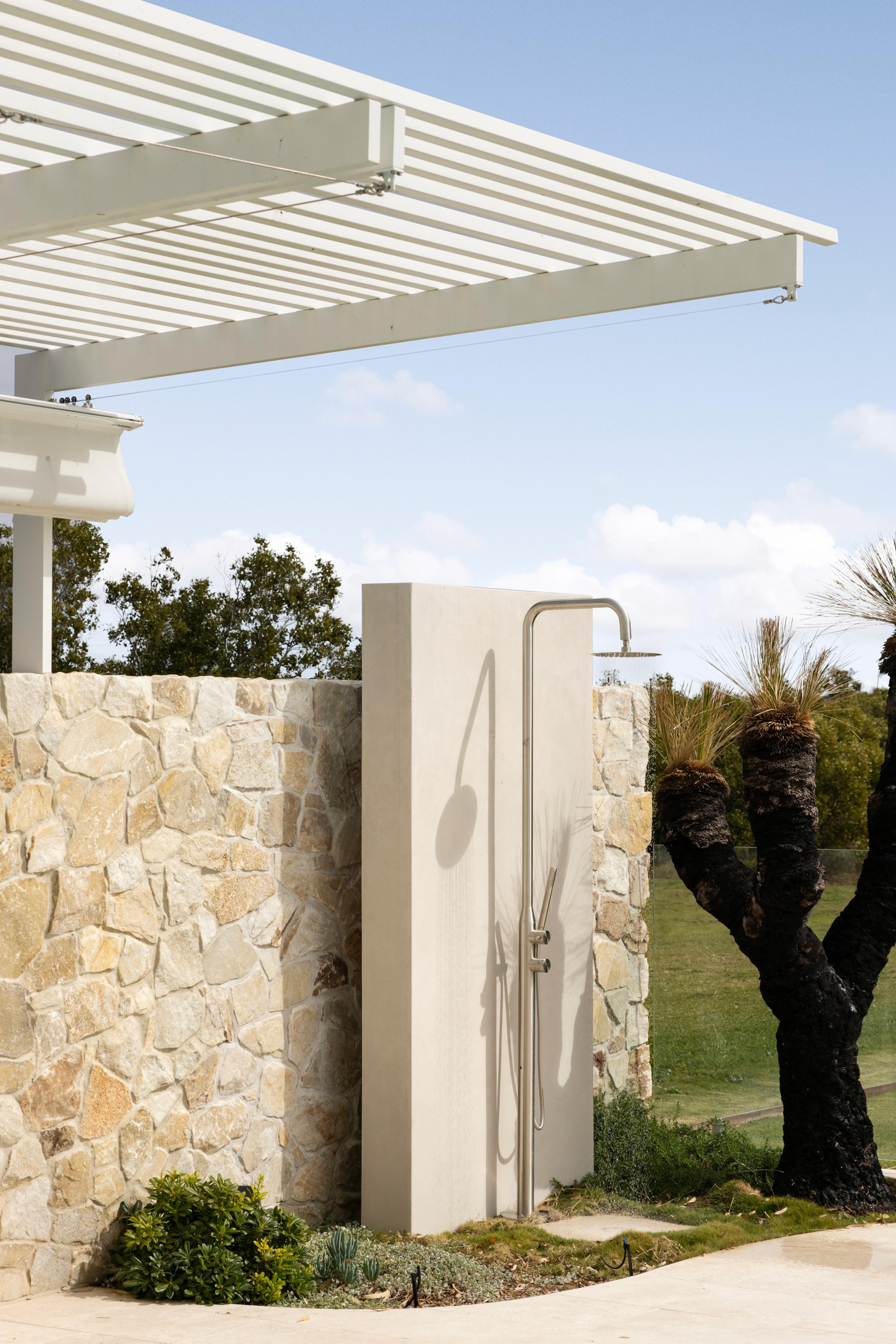Outdoor shower against stone wall under louvred pergola