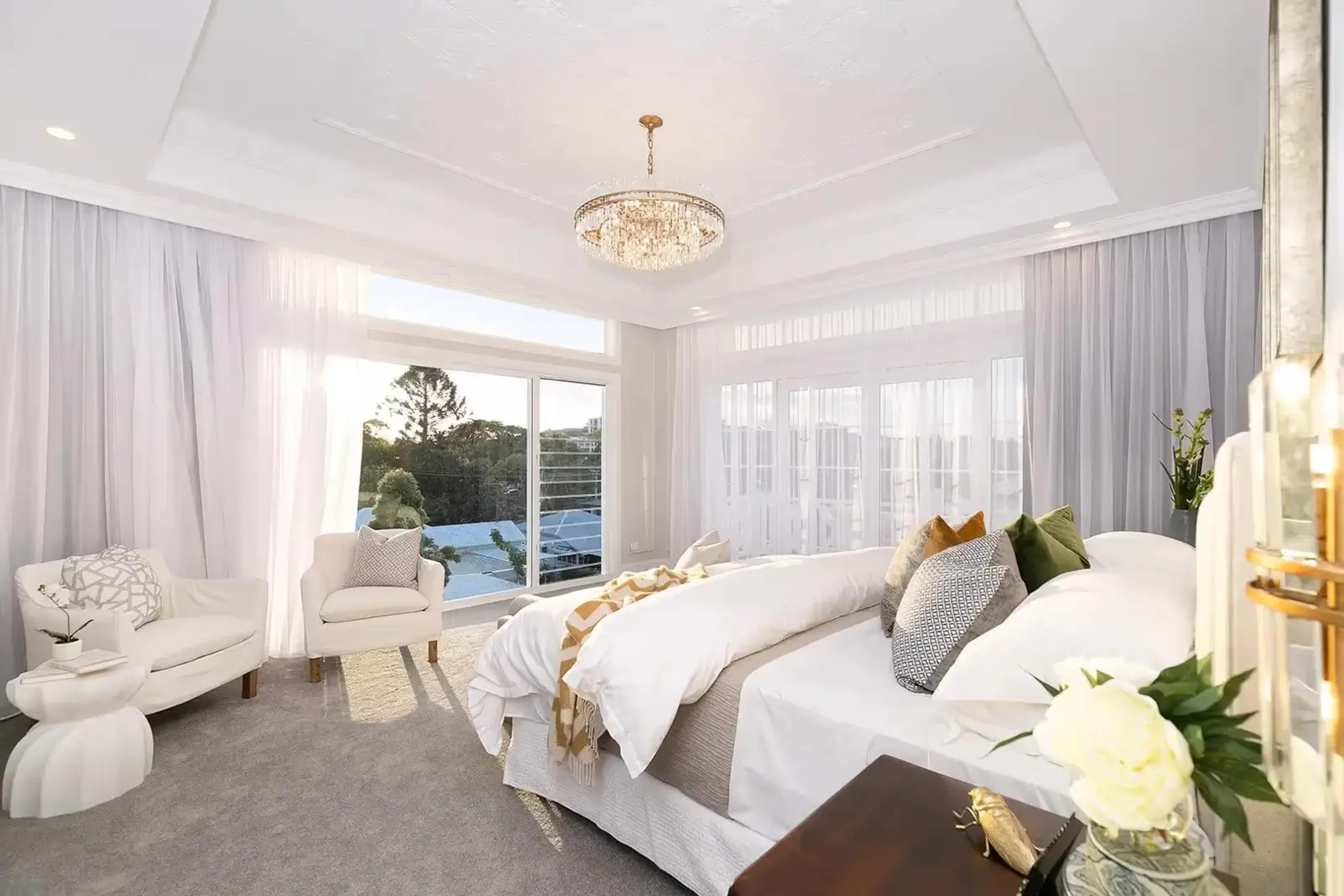Main bedroom with chandelier, sheer curtains and leafy outlook