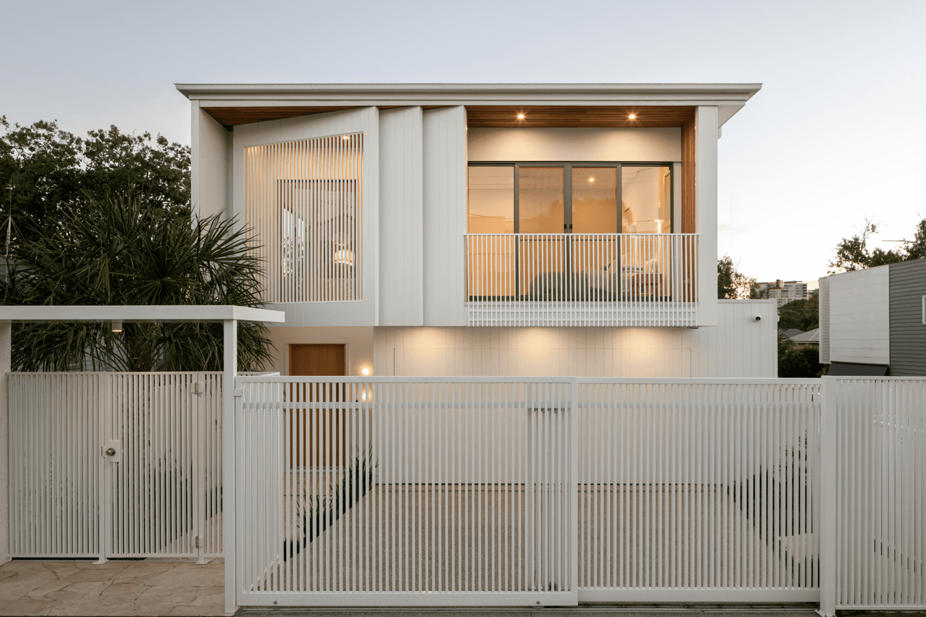 Street facade of white two storey house behind slatted gates at dusk