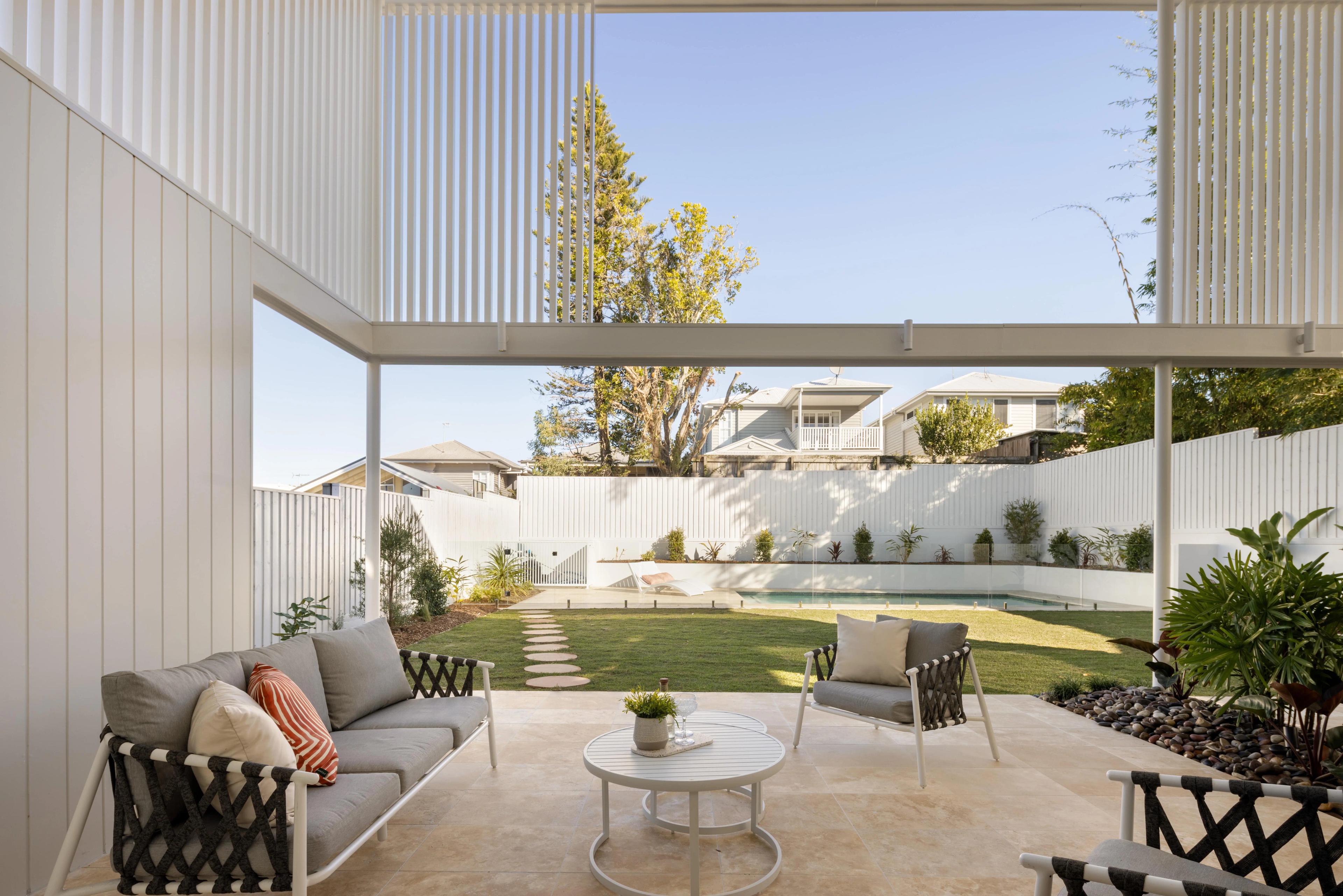 Covered outdoor lounge overlooking landscaped backyard and pool