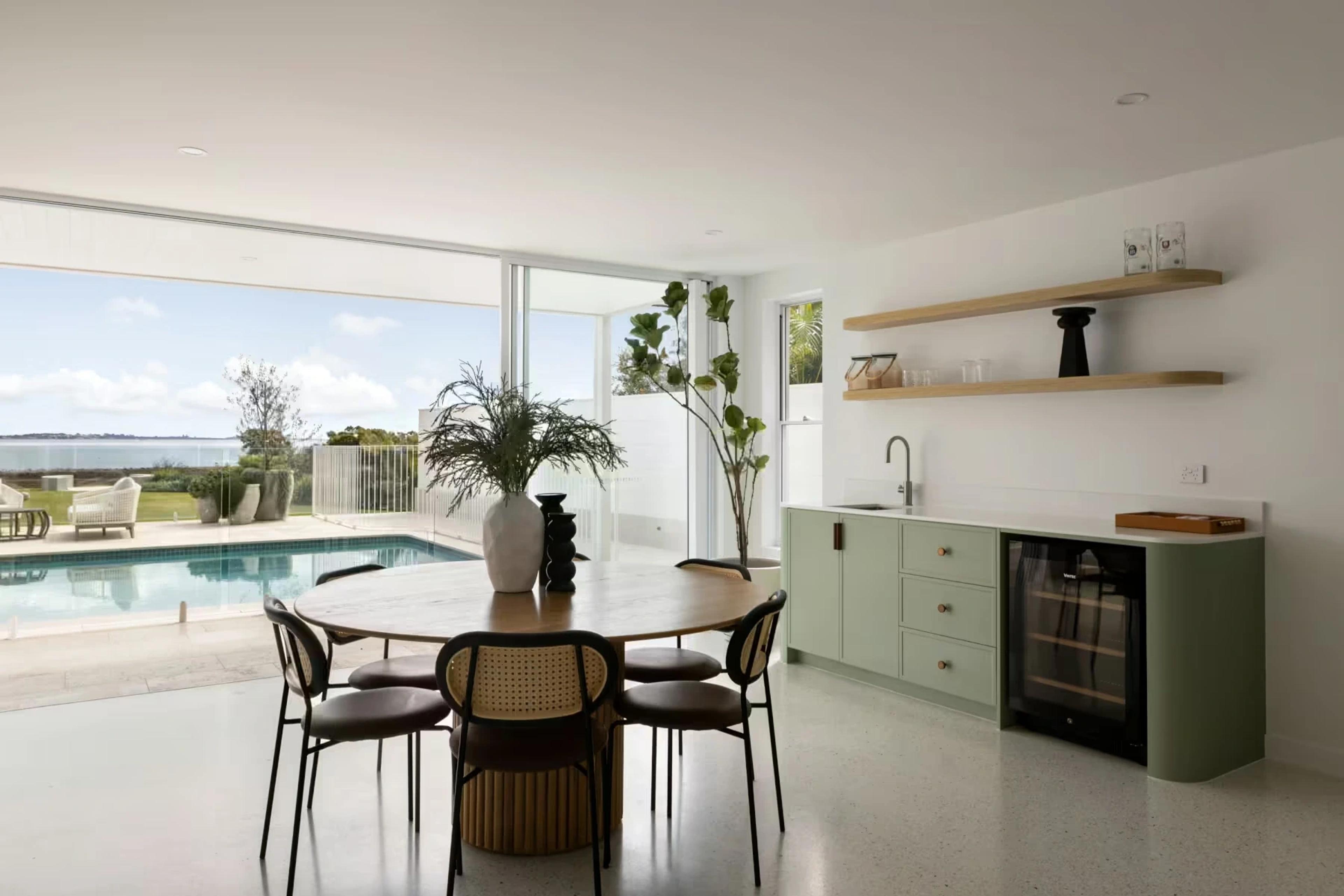 Dining area and bar with green cabinetry beside pool