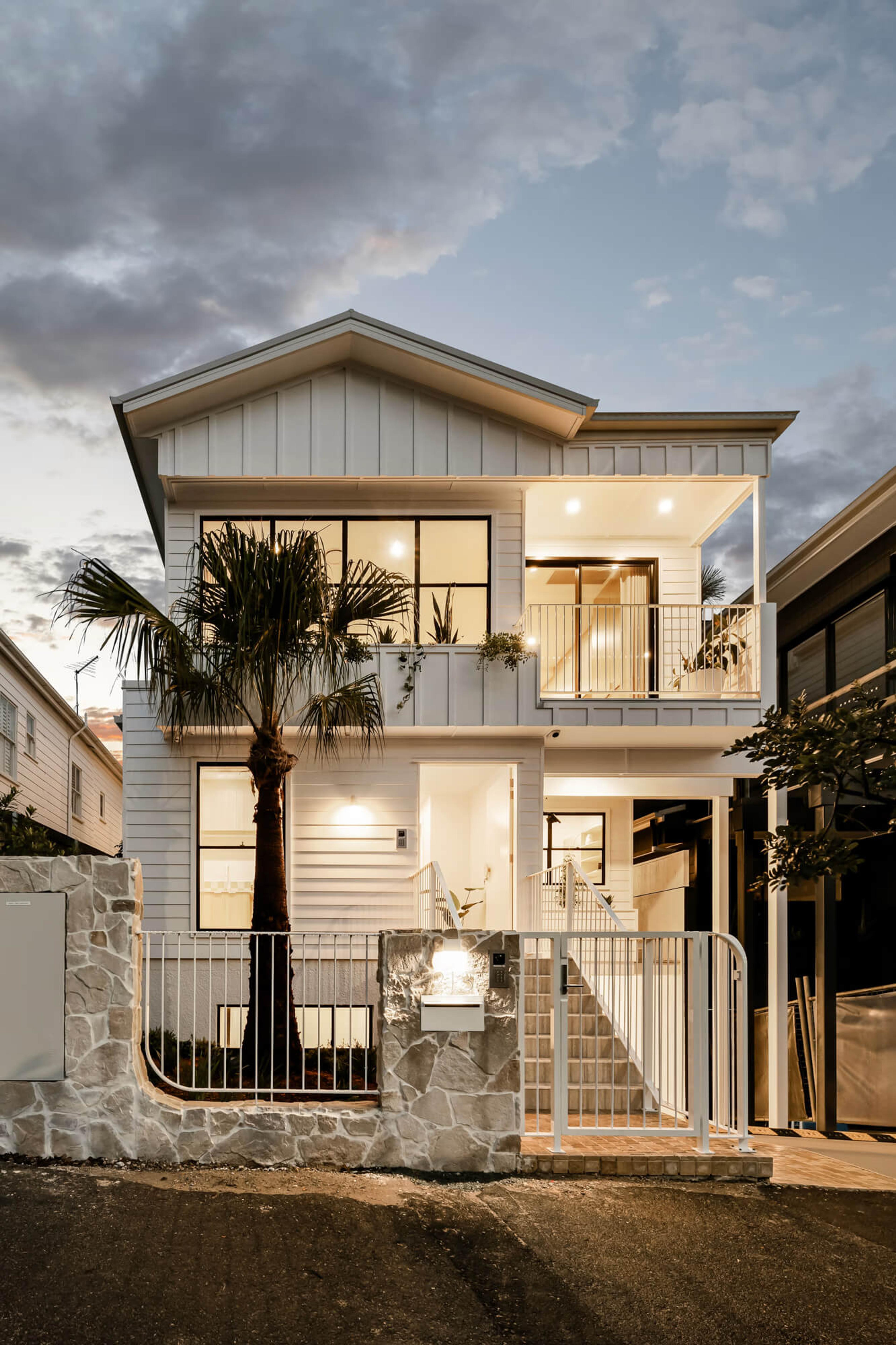 Two storey townhouse street facade with balcony and stone front wall at dusk