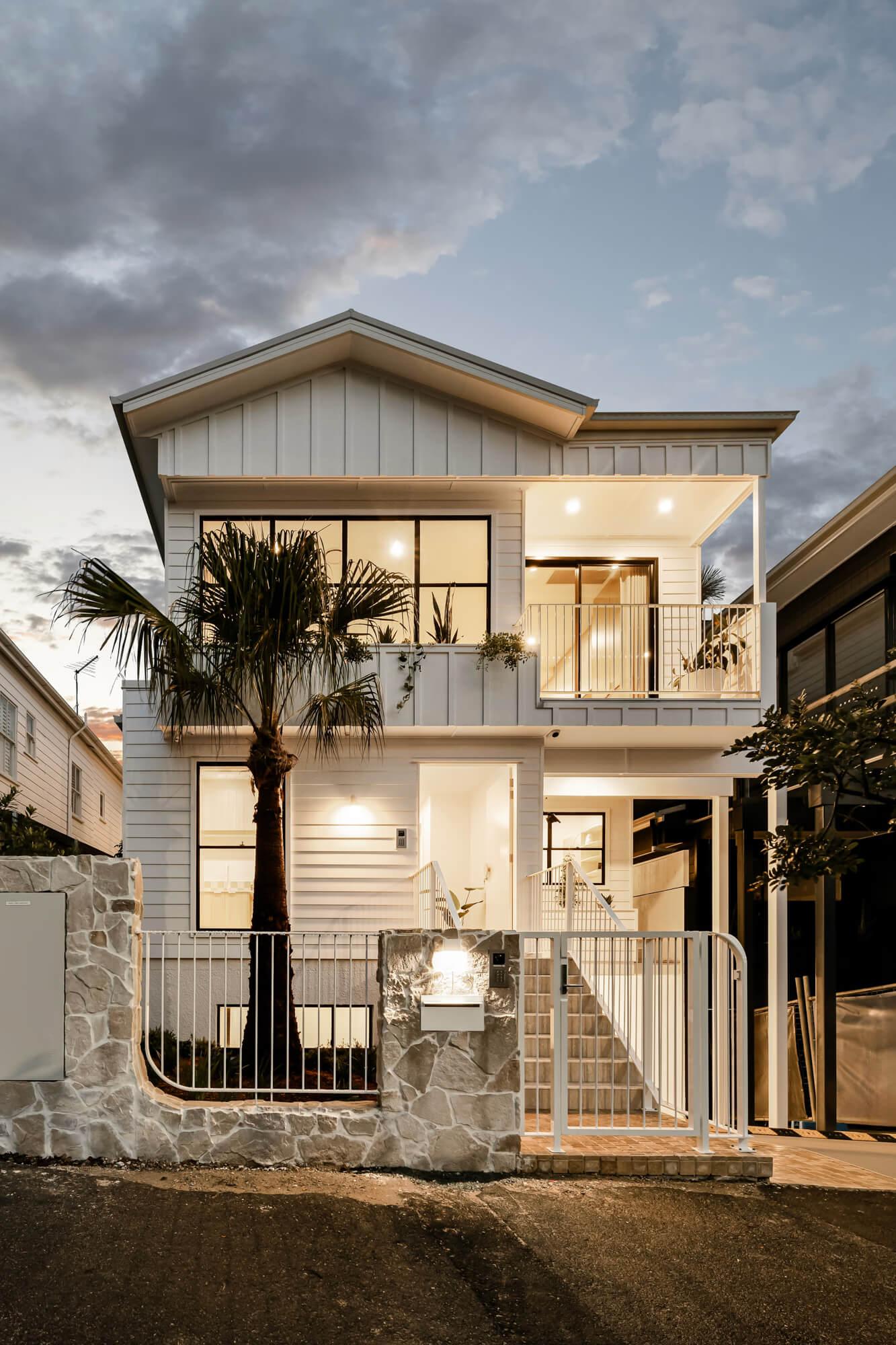 Two storey townhouse street facade with balcony and stone front wall at dusk