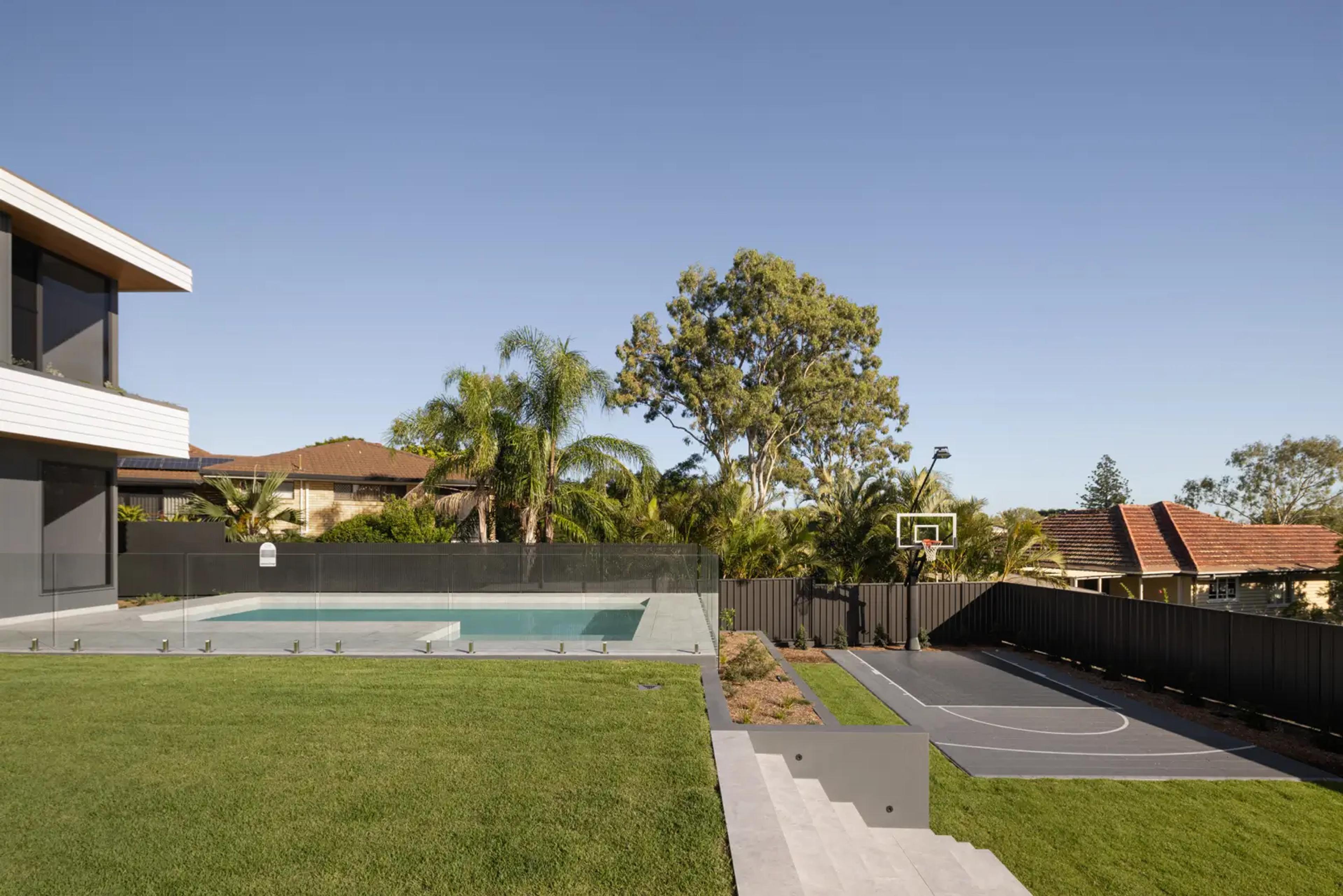 Backyard pool, lawn and basketball court beside timber fence