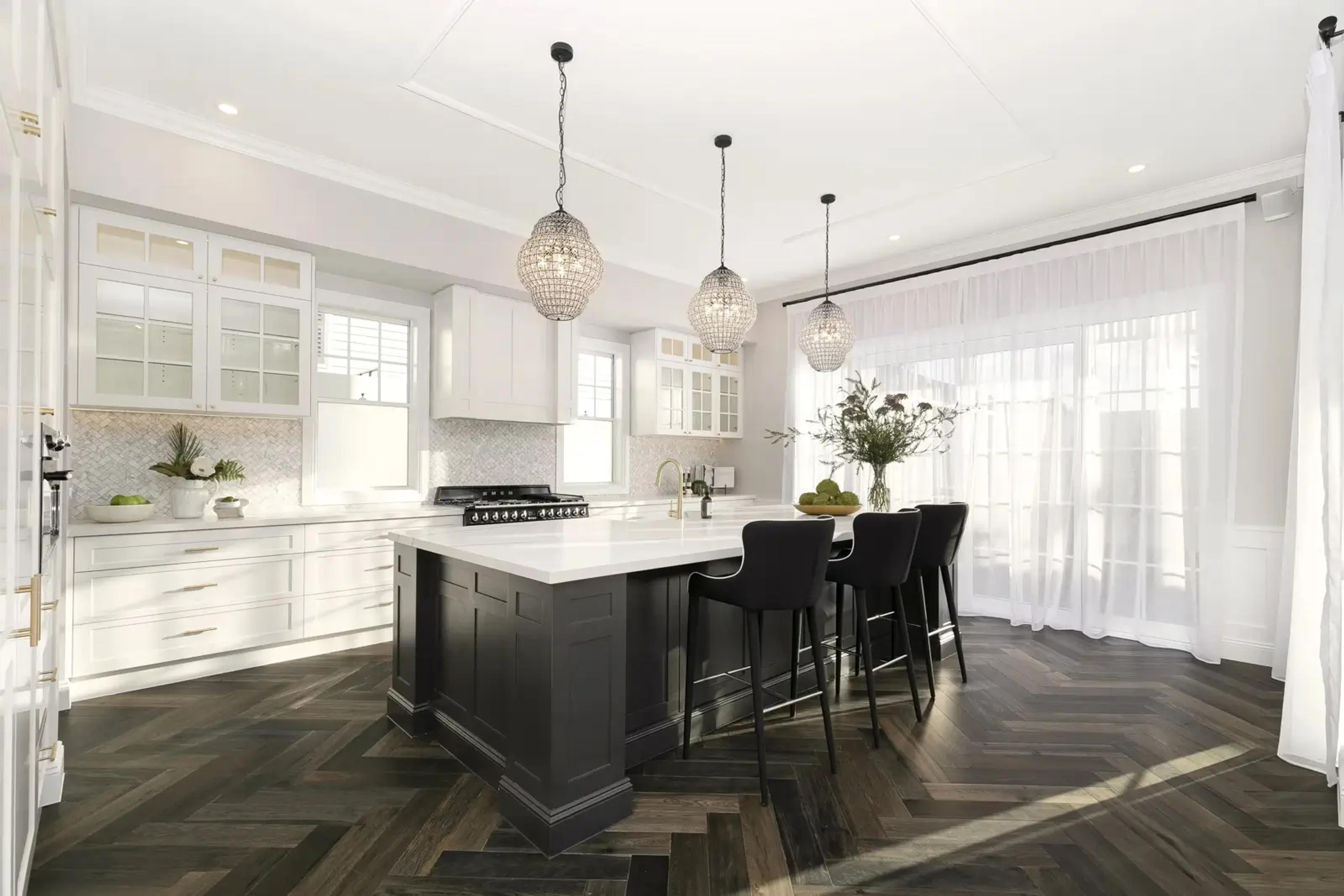 White kitchen with black island, pendant lights and herringbone floor