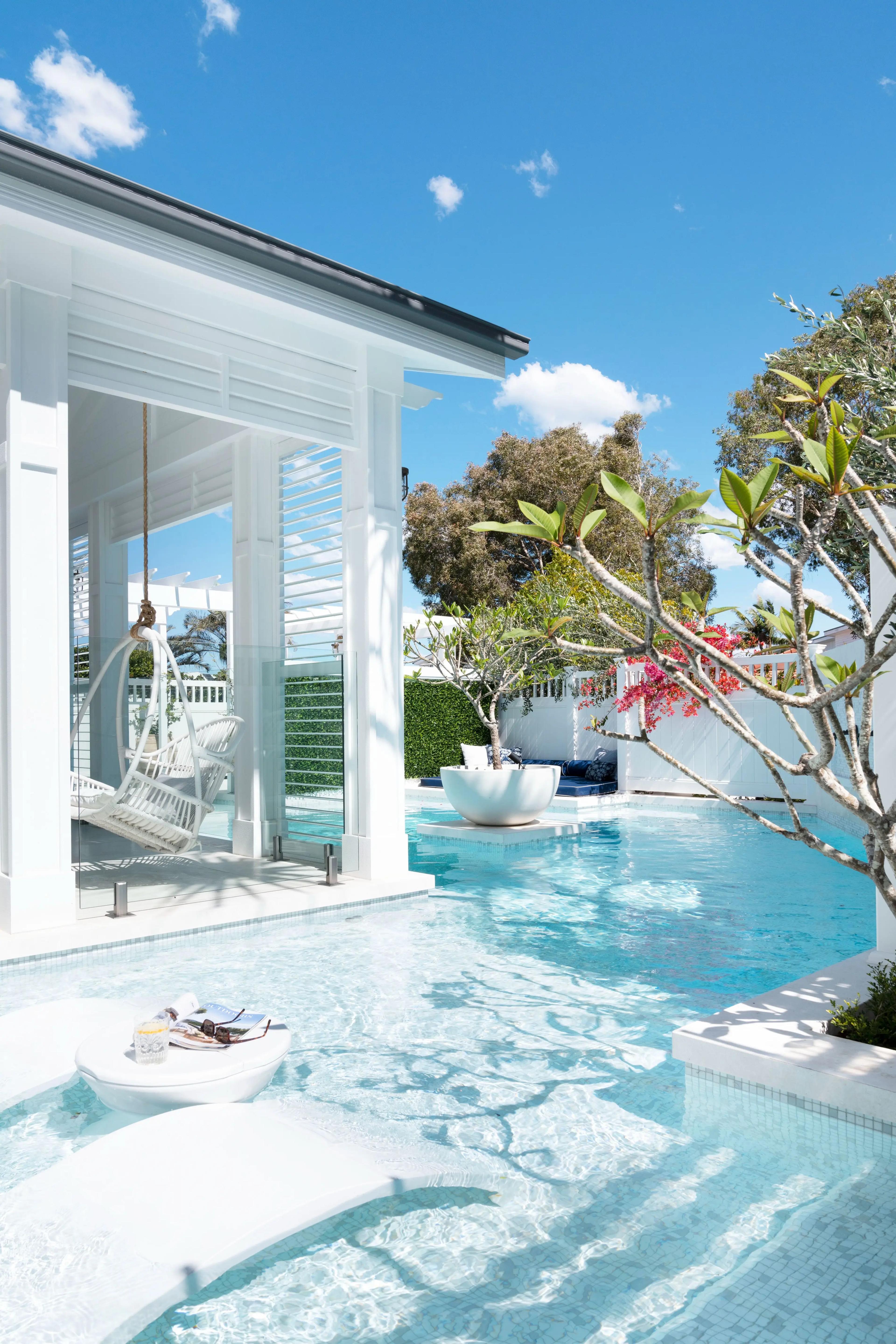 Poolside cabana with hanging chair beside bright blue swimming pool