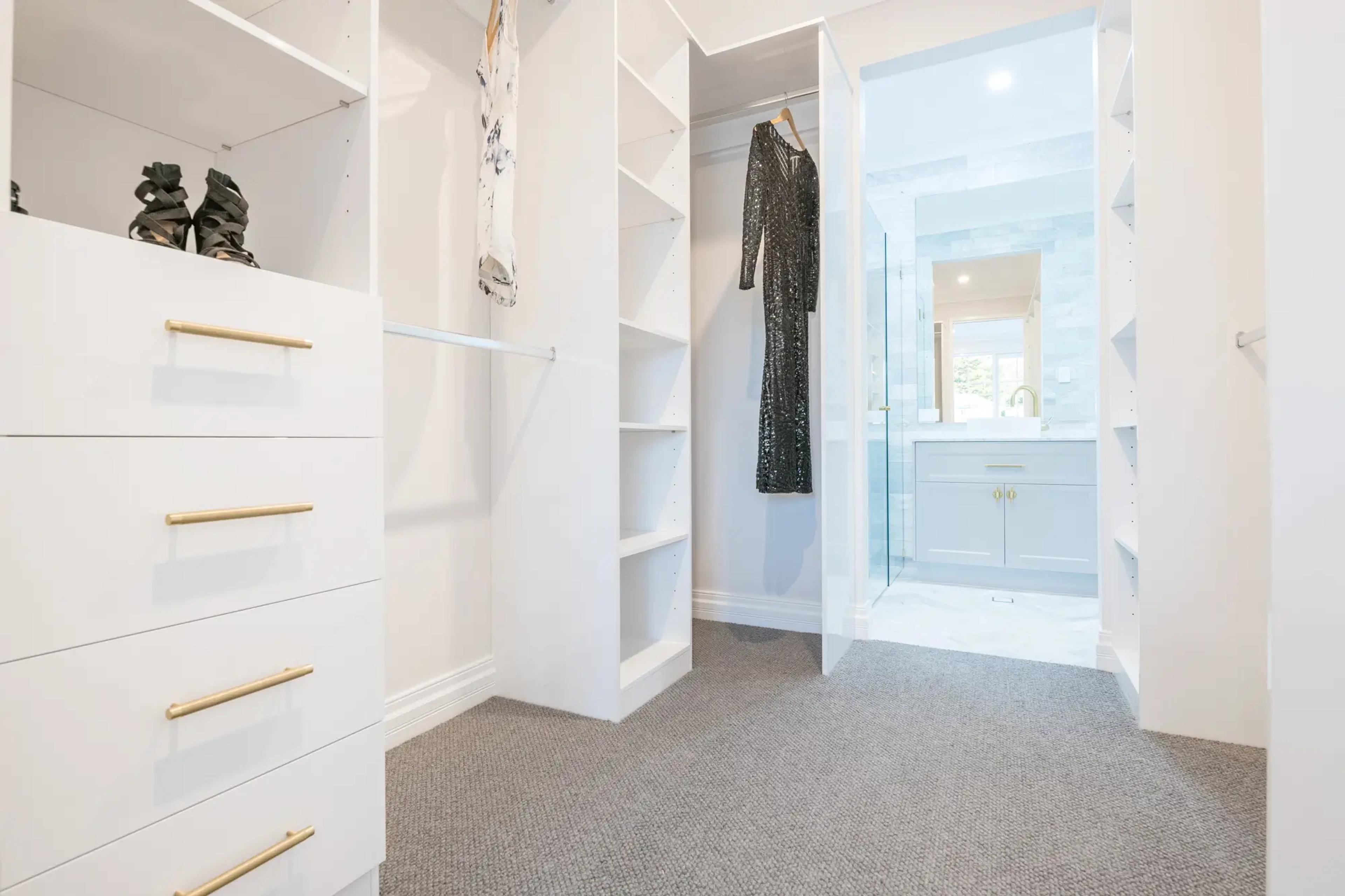Walk in wardrobe with white shelving leading to ensuite