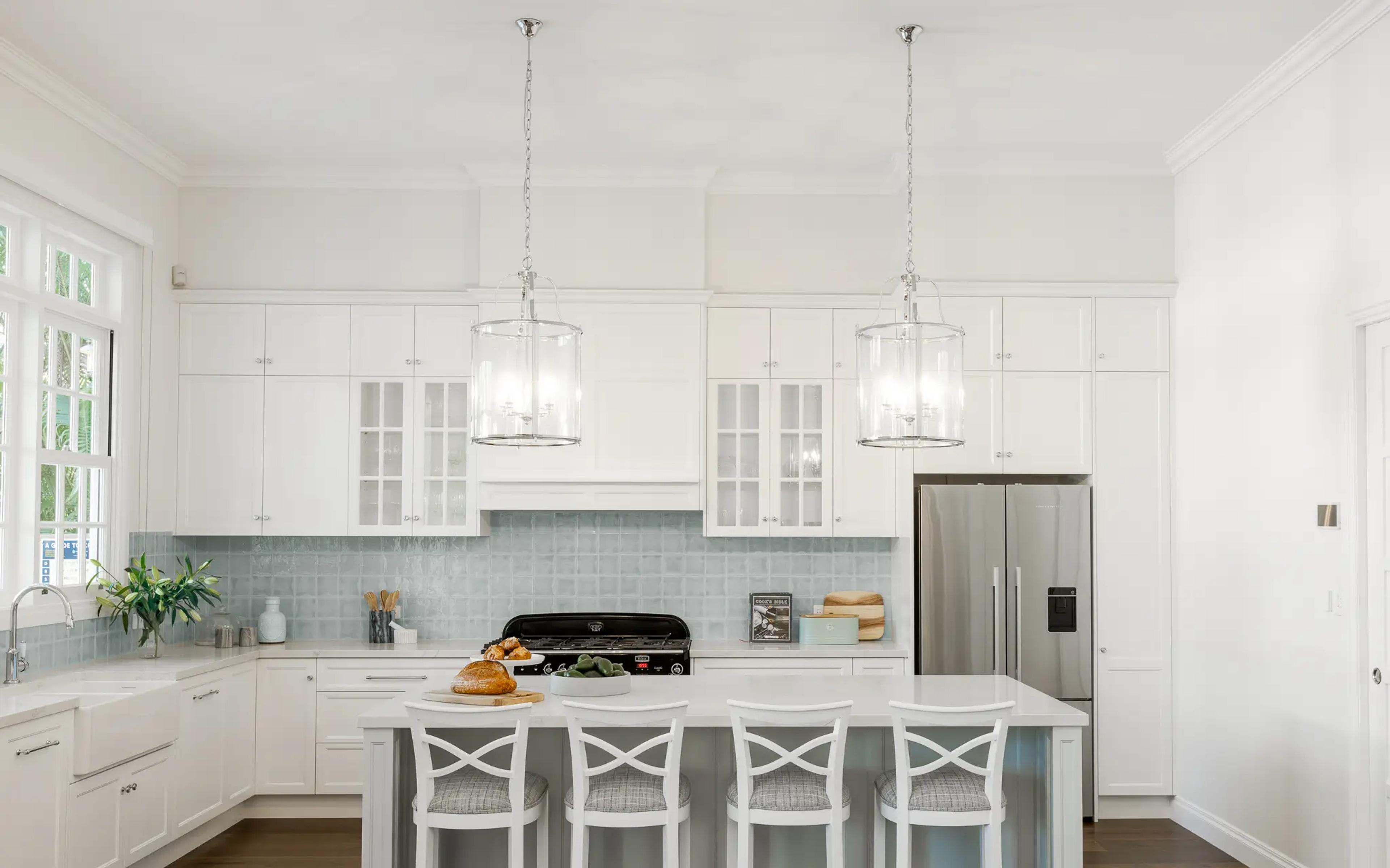 White kitchen with island bench, glass pendant lights and pale blue splashback