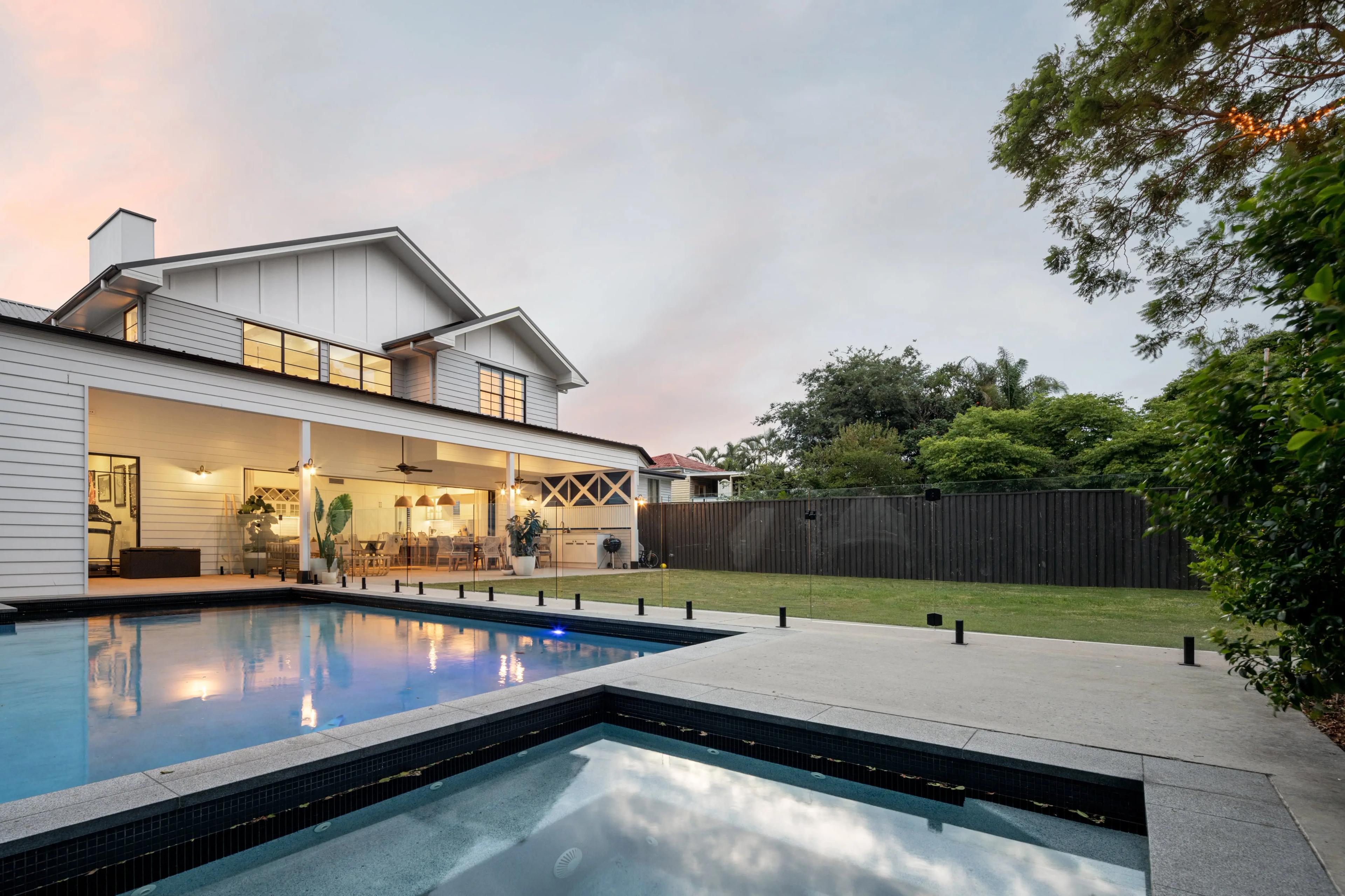 Backyard pool and spa with lawn beside the home at dusk