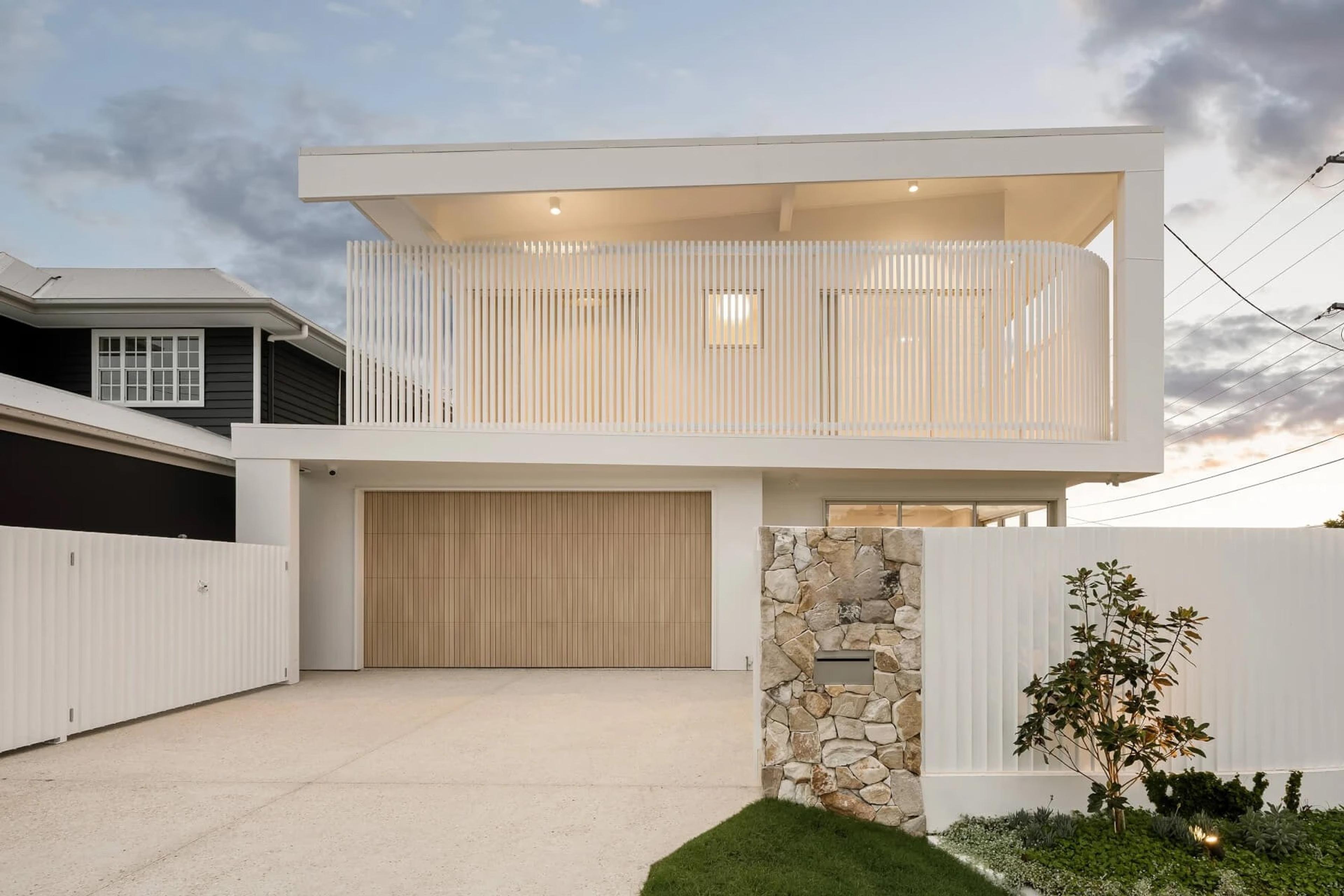 White two storey home street facade with garage and stone wall