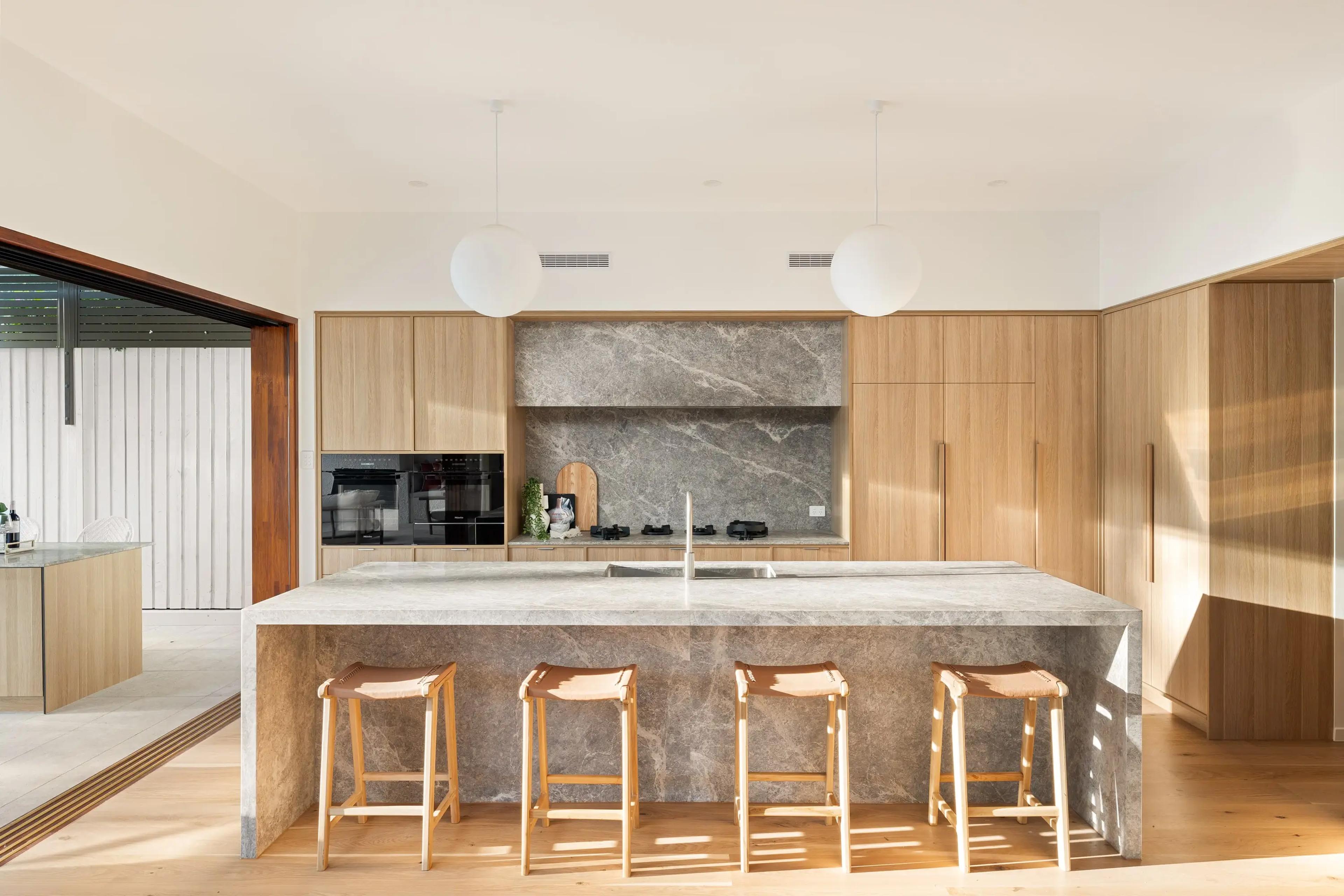 Kitchen with stone island bench, timber joinery and pendant lights