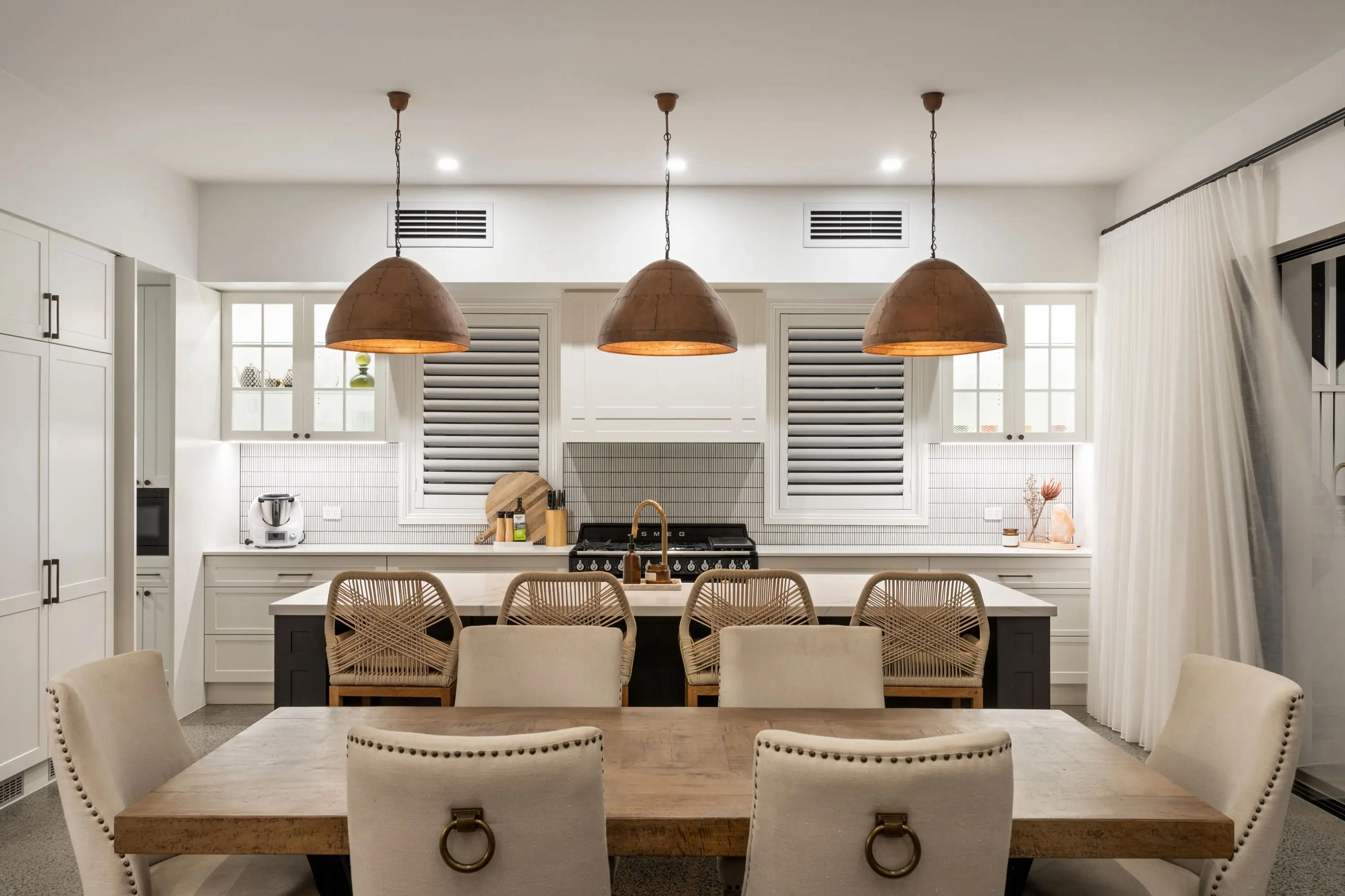 White kitchen with island bench and three pendant lights over dining table