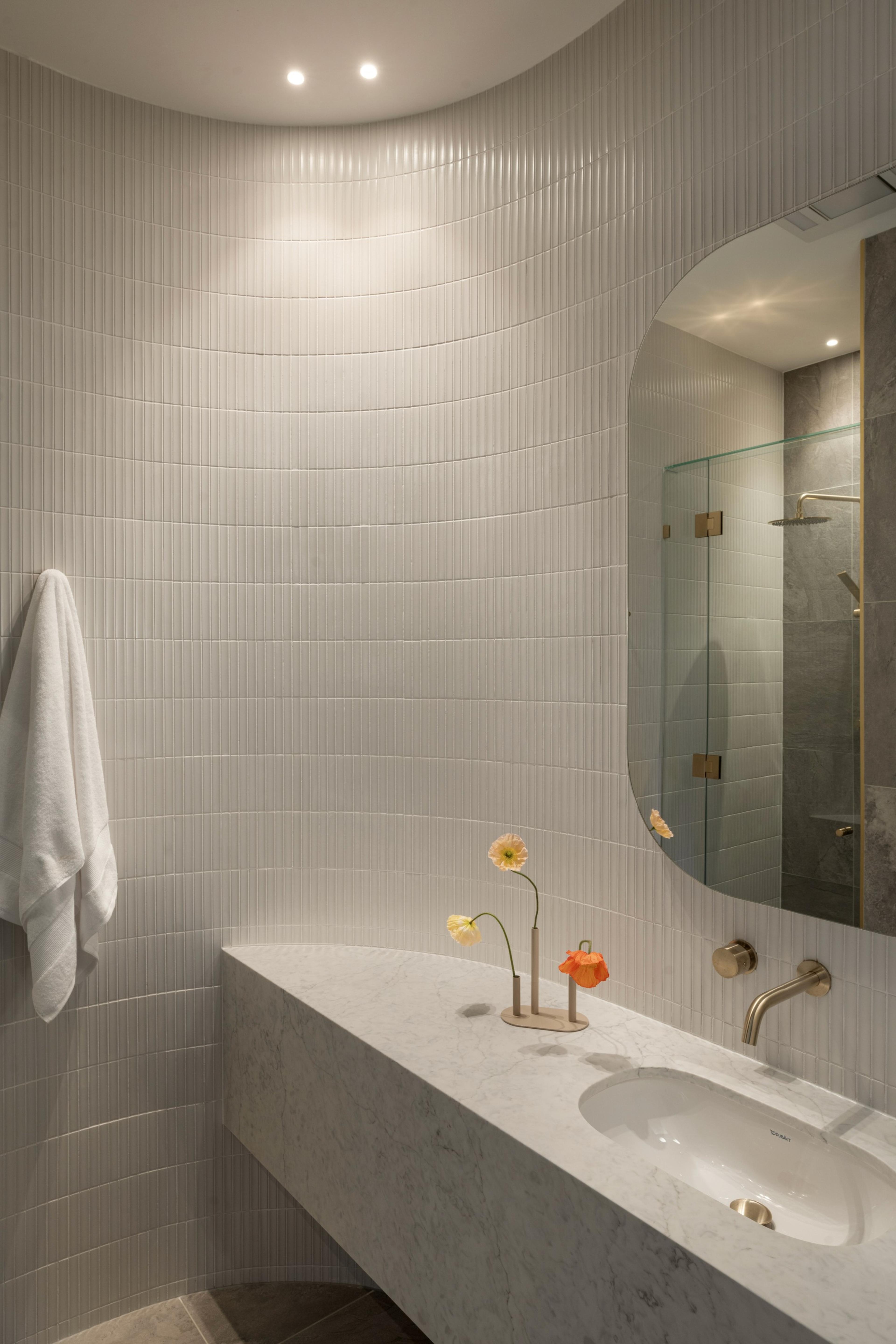 Curved powder room with fluted white tiles and marble vanity