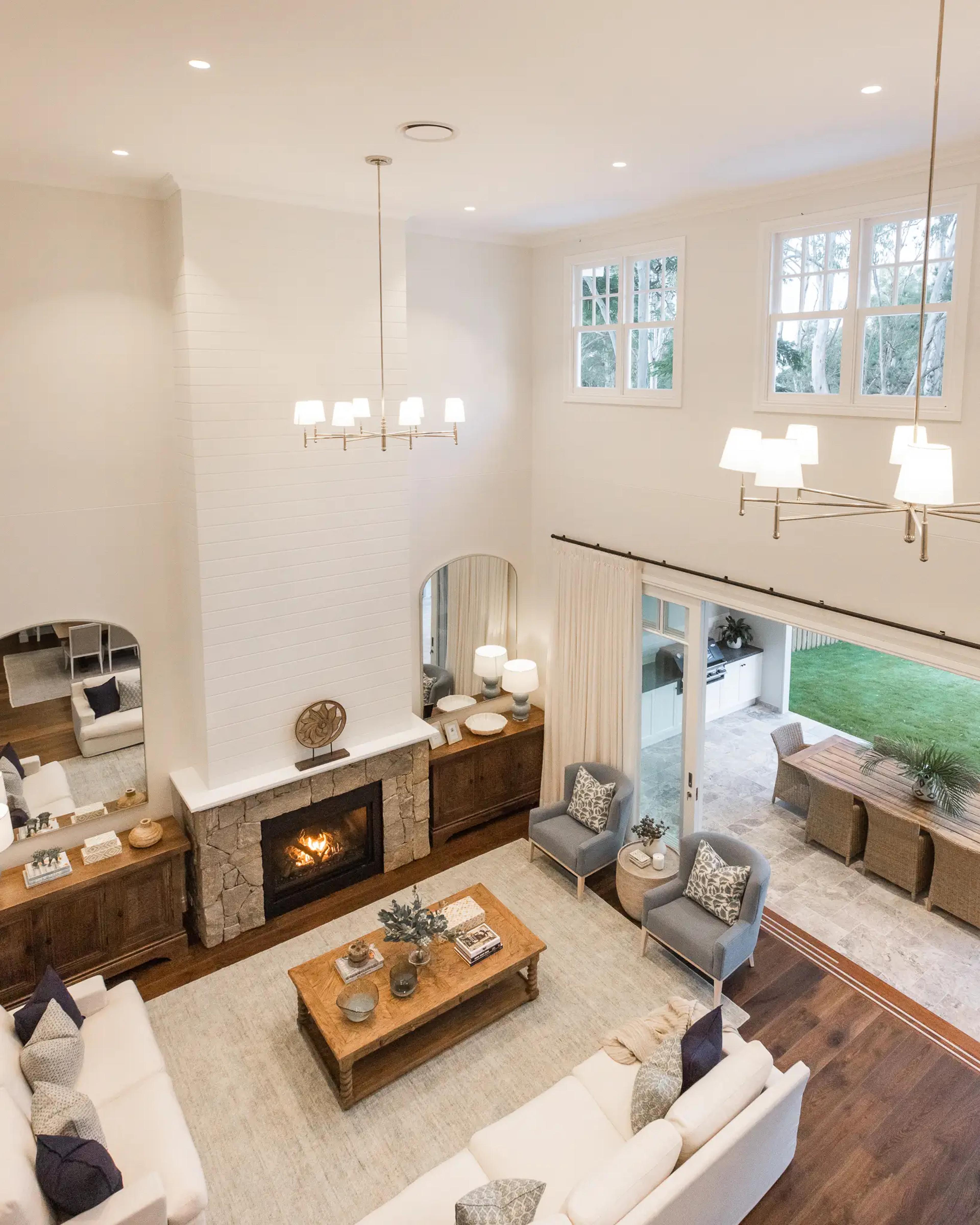 Double height living room with stone fireplace, brass chandeliers and cream sofas