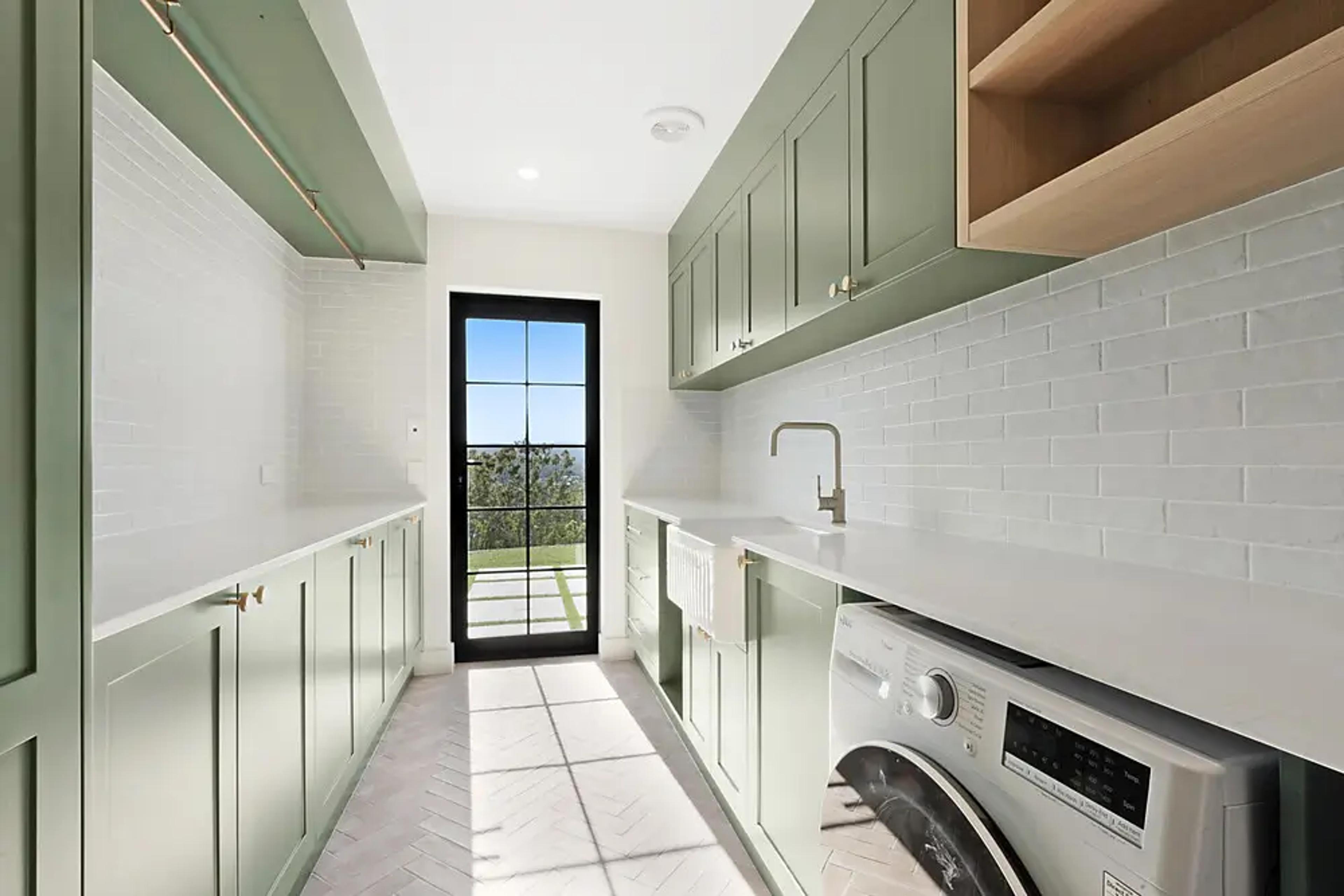 Laundry with sage green cabinets, subway tiles and glass door.