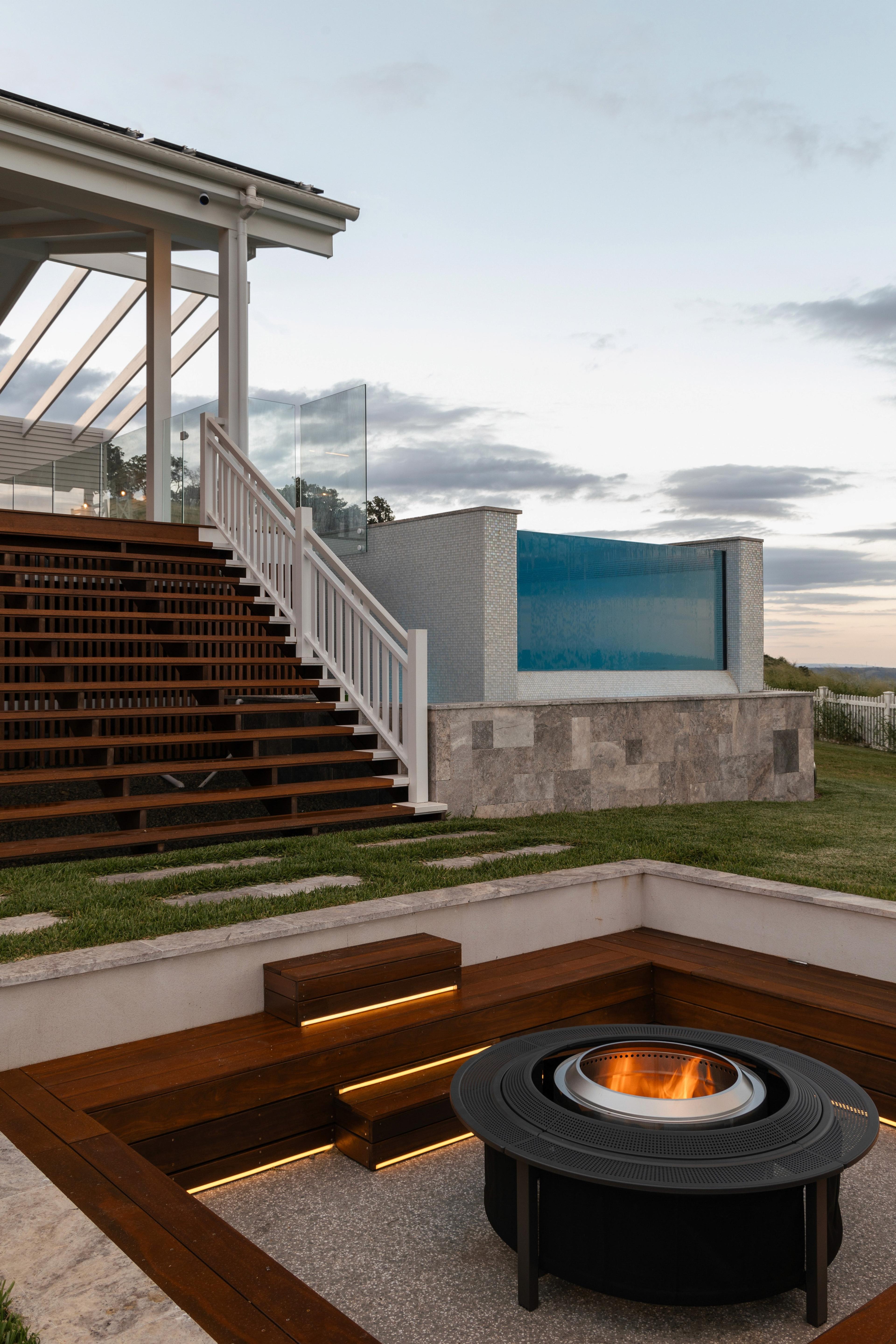 Timber deck stairs beside glass pool and sunken fire pit