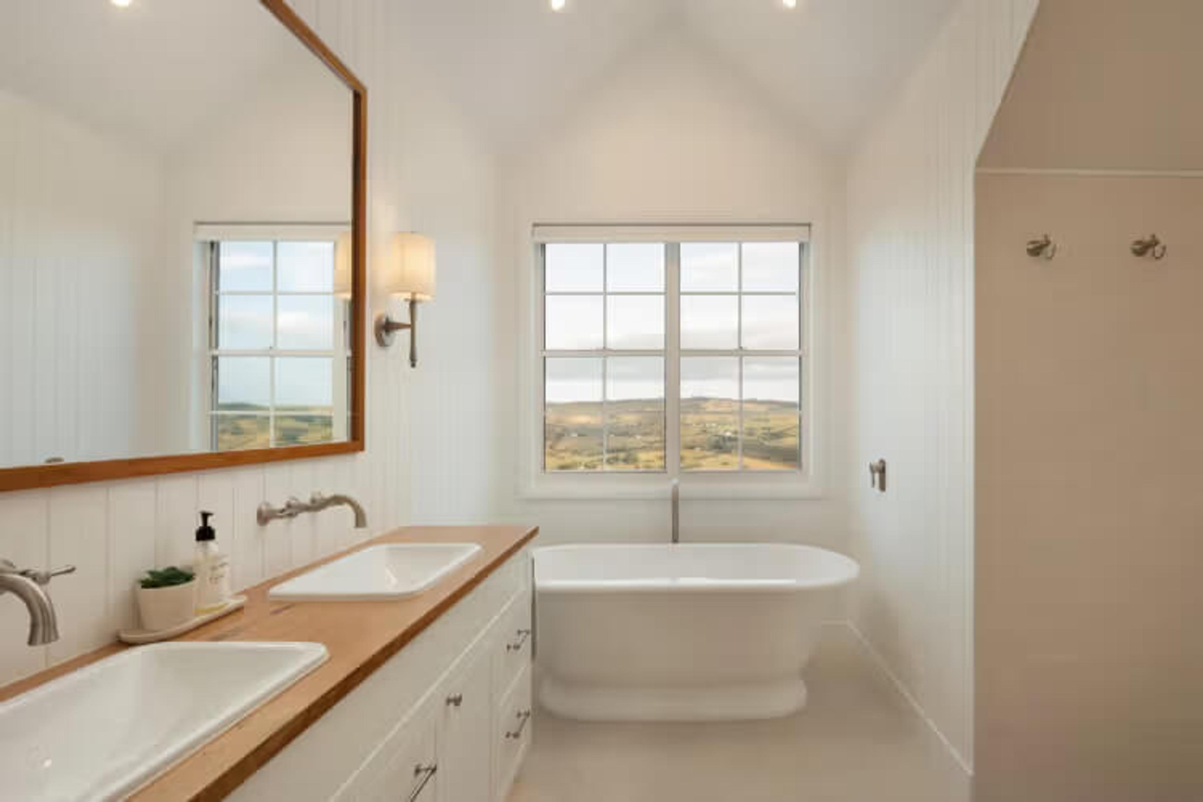 Freestanding bath beneath a window with a rural outlook and timber-topped double vanity, Illalangi in Bunburra, by Invilla Architecture