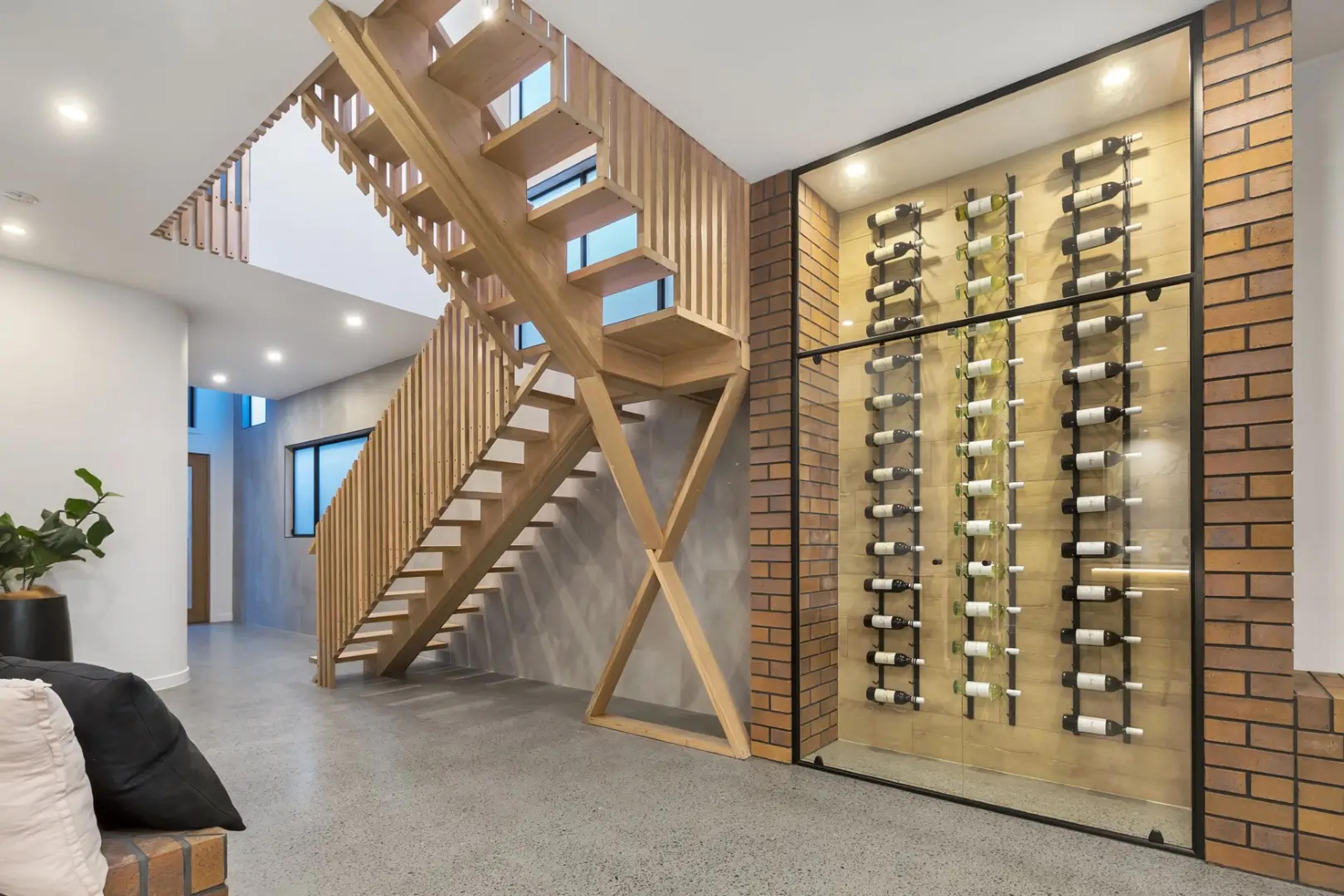 Floating timber staircase beside glass fronted brick wine cellar